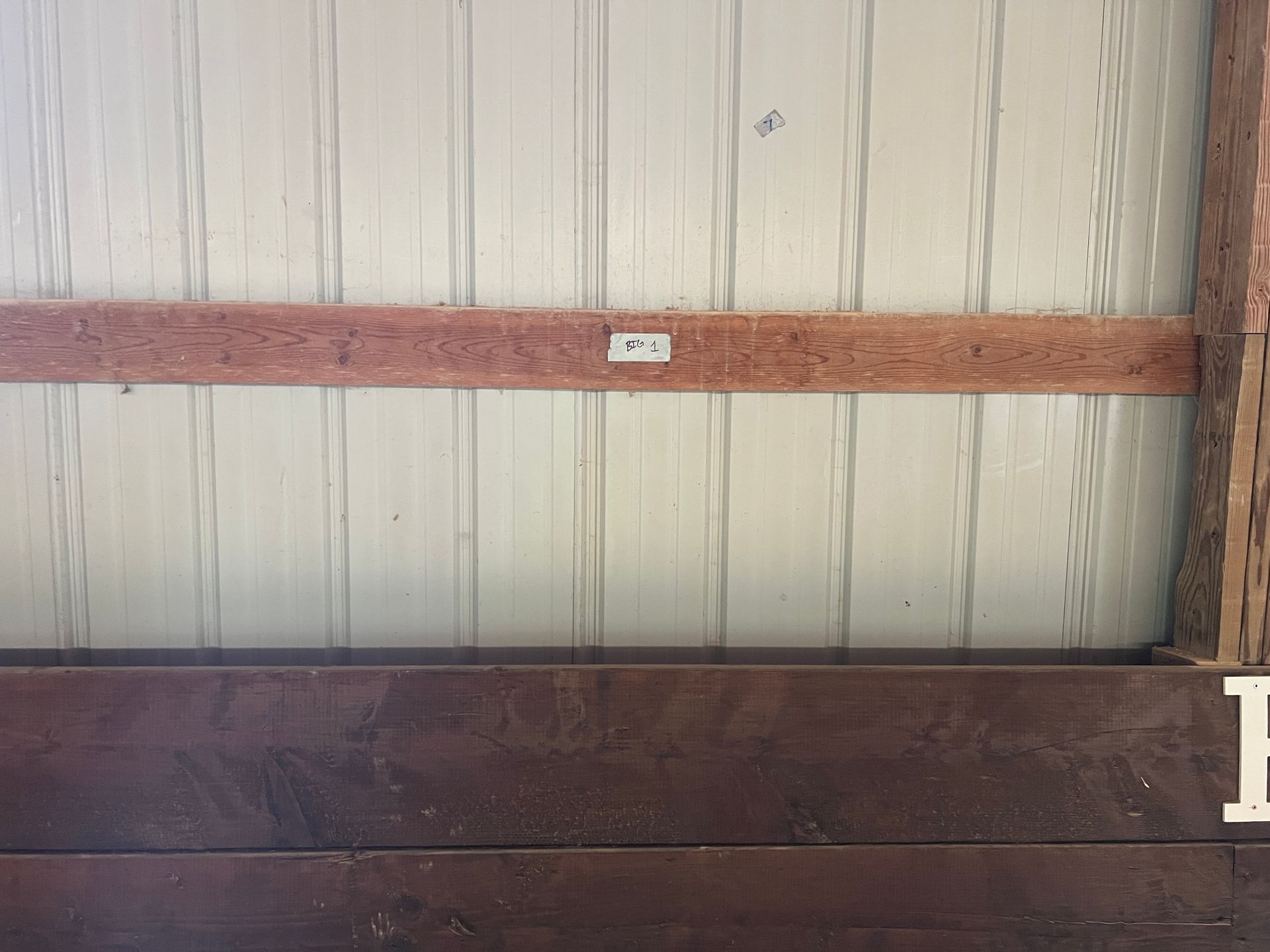 A wall with white metal siding, a horizontal wooden board, and dark brown wood planks at the bottom.