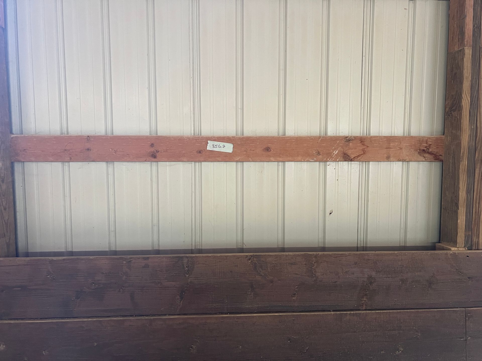 A white metal wall panel framed by dark horizontal wooden beams, with a small white tag attached to the center beam.