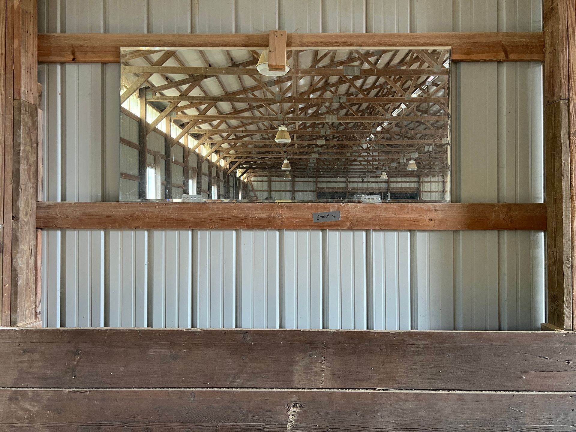 A large, rectangular mirror mounted on a corrugated metal wall between horizontal wooden support beams.
