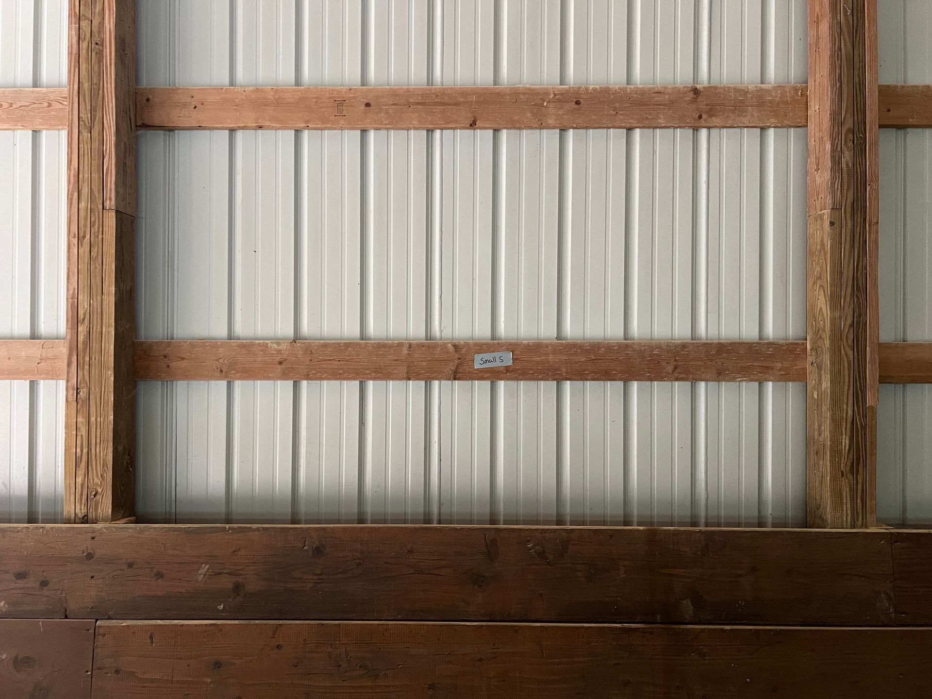 A light-colored corrugated metal wall framed by vertical wooden posts and horizontal wooden slats, with dark wood paneling.