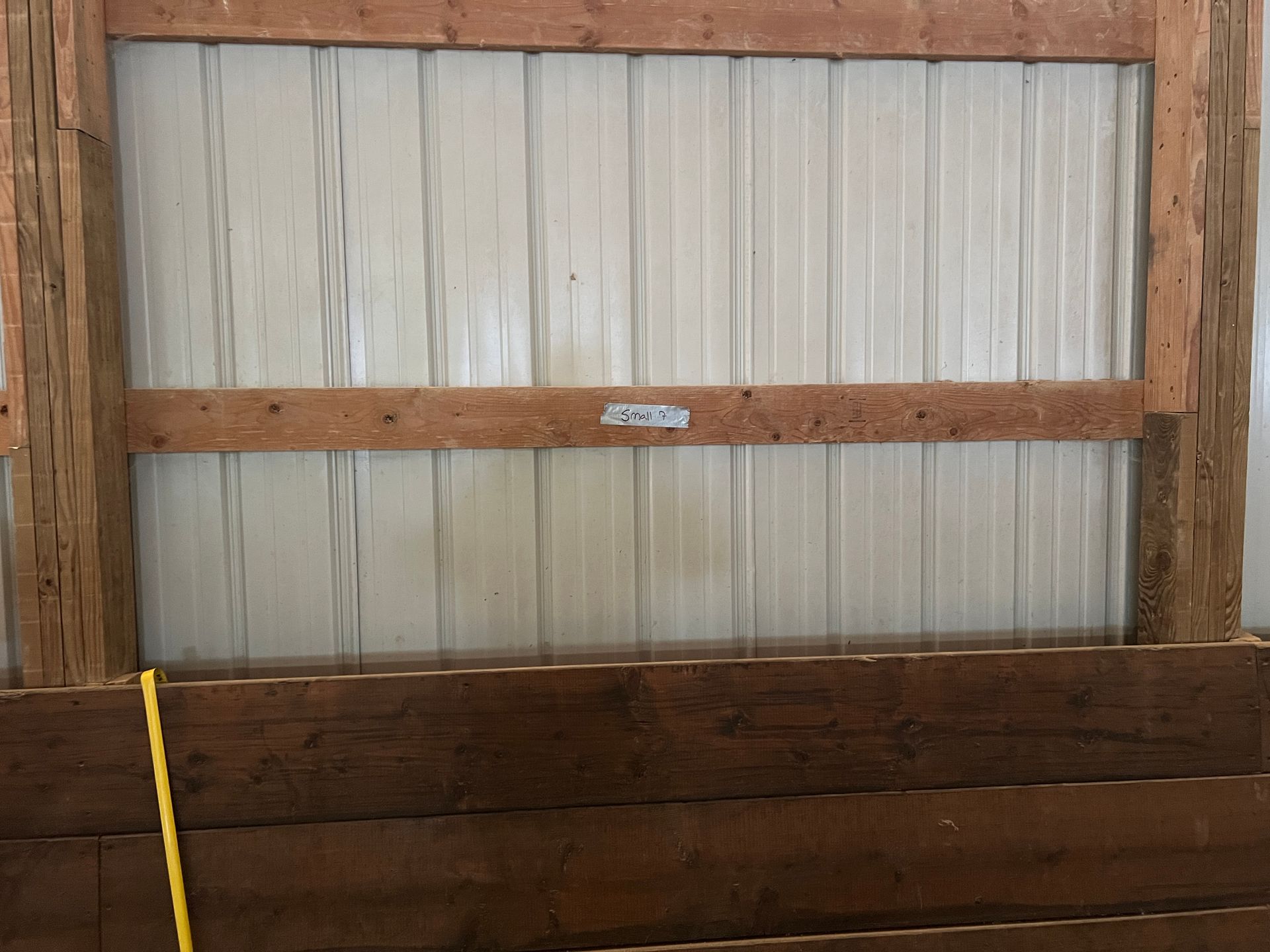 White metal wall paneling with wooden beams and lower horizontal wooden planks in a rustic or agricultural structure.
