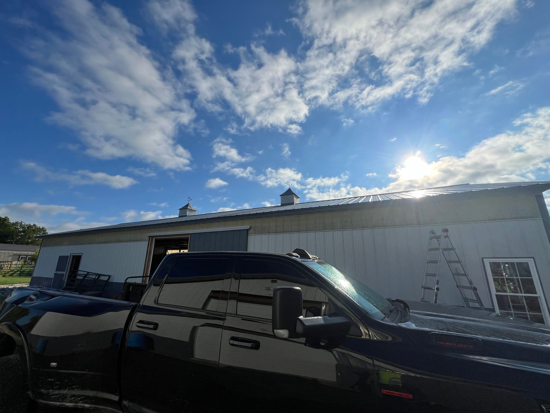 A black truck parked in front of a white building under construction with a ladder against the wall under a sunny sky.