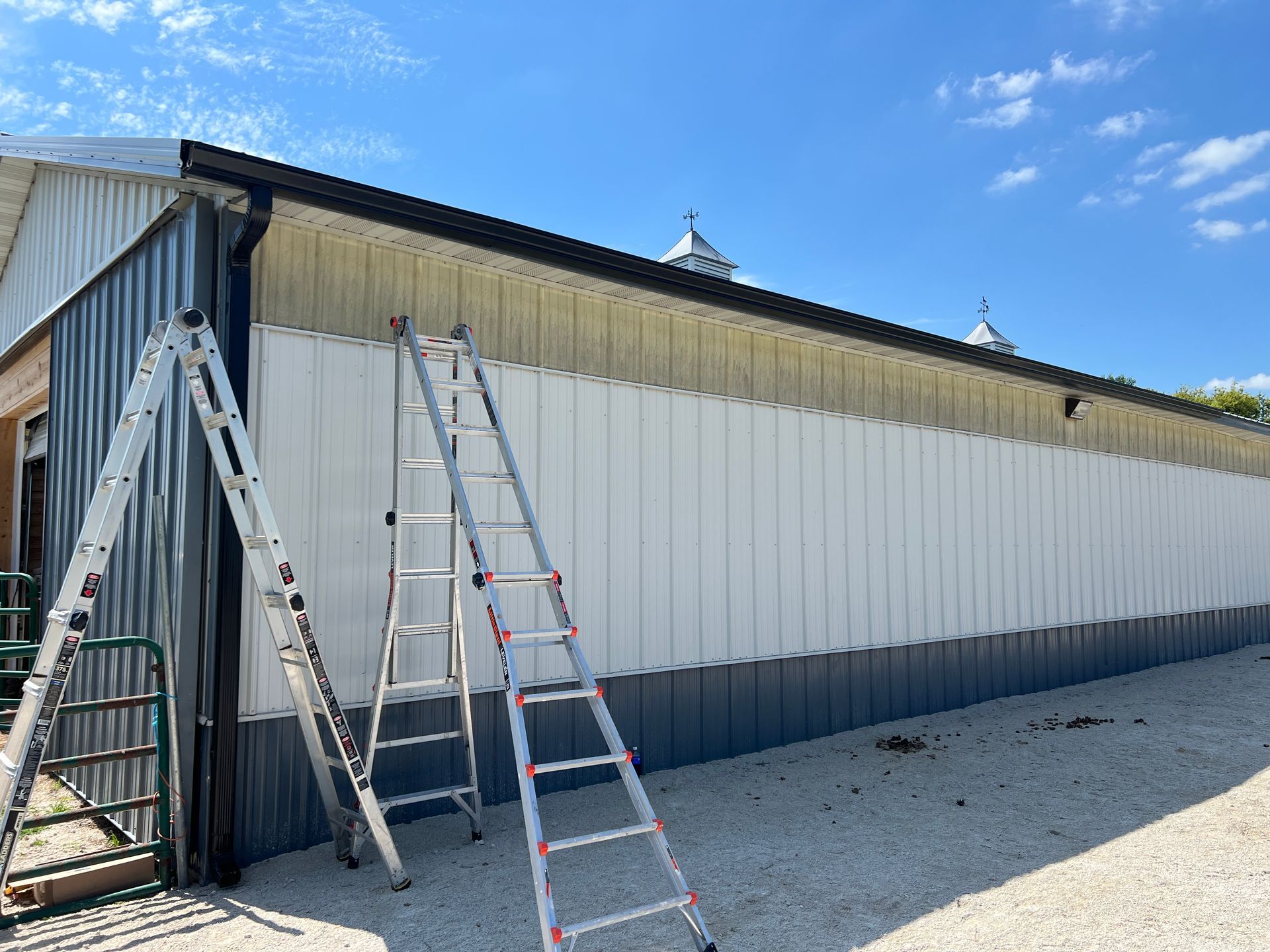 A ladder leans against the side of a metal-sided building with white panels being installed over the original siding.