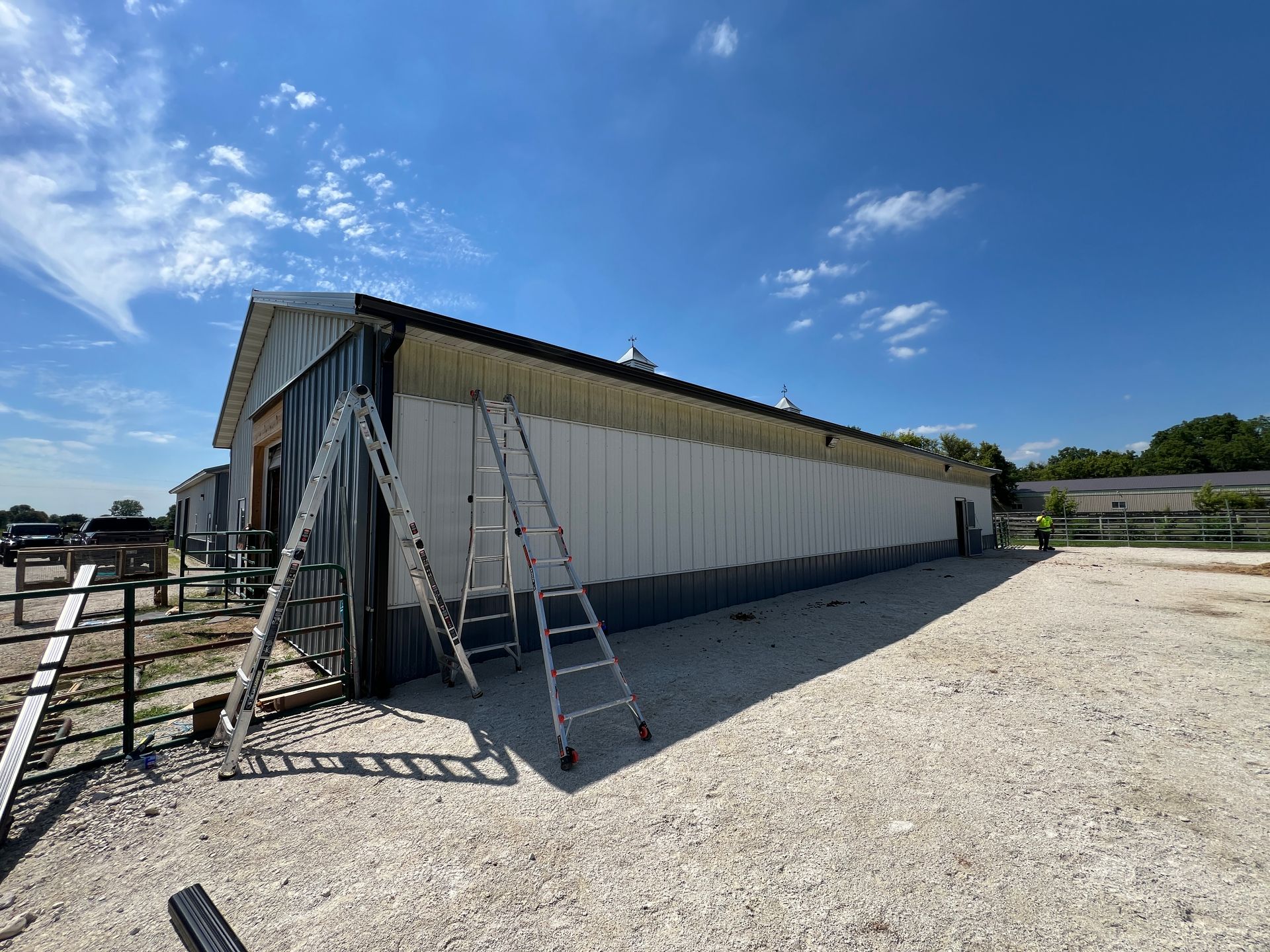 Two metal ladders stand against the side of a large, white-sided industrial building under a bright blue sky.