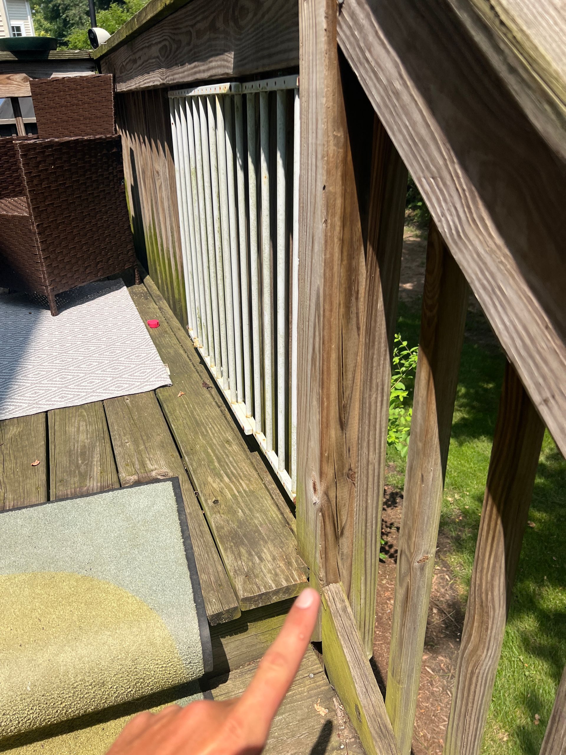 A close-up view of a wooden deck railing with a white gate, with a finger pointing to a gap near the post.