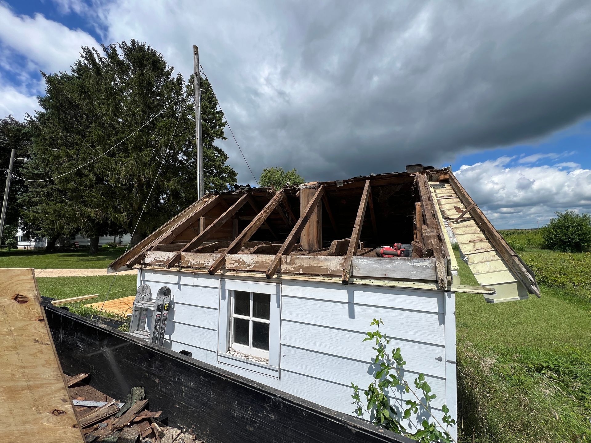 A small, white, siding-covered building with an open-roof frame under a cloudy sky.