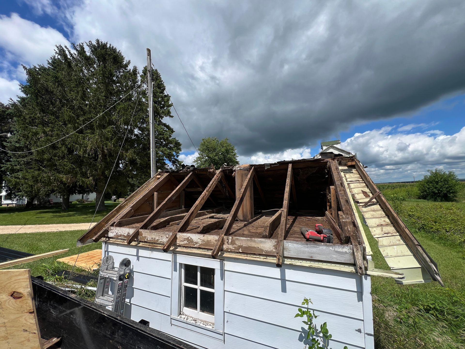 A small white building with a shed roof under construction, showing exposed wooden rafters against a partly cloudy sky.