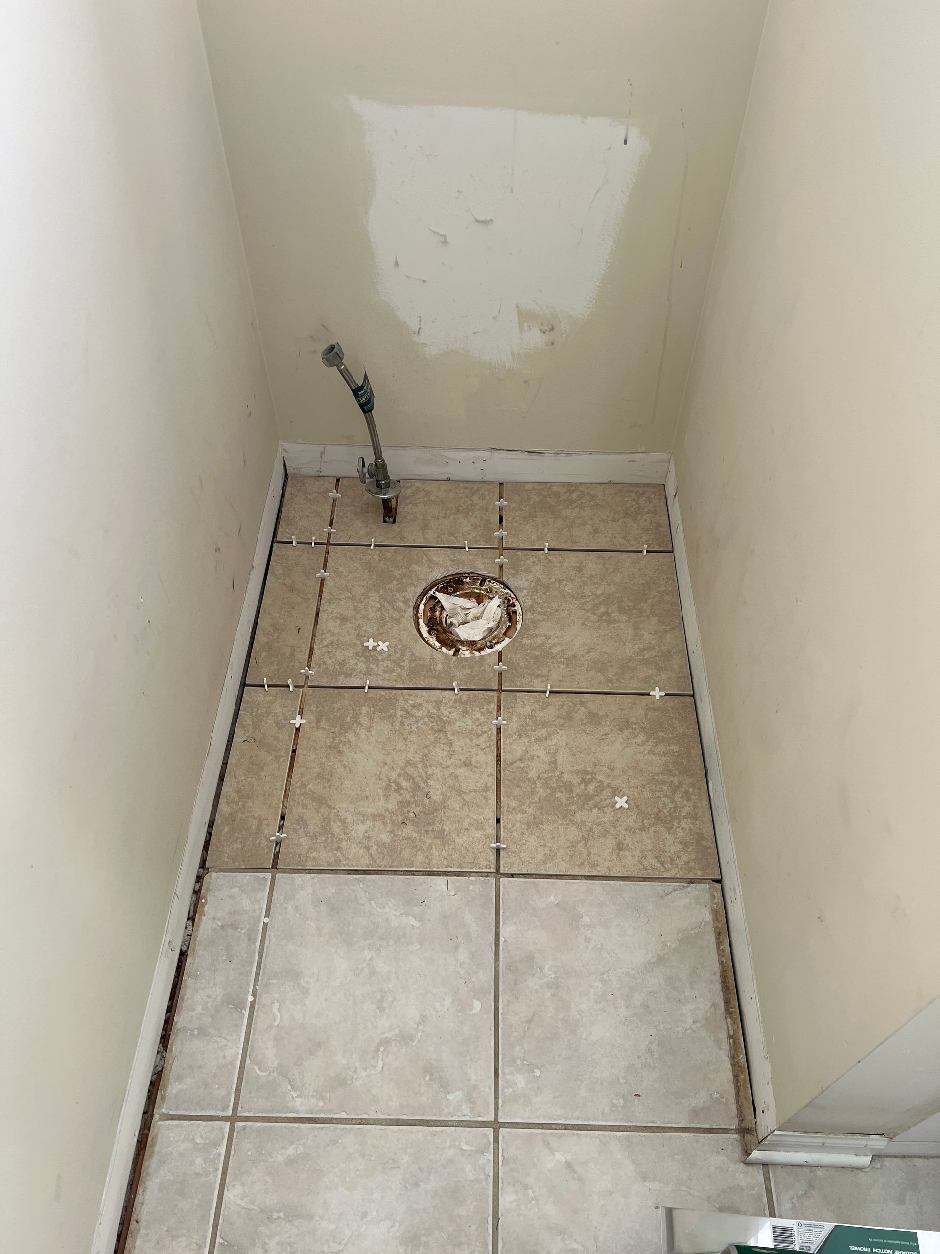 A small bathroom floor undergoing renovation with freshly laid tiles, a toilet flange, and a water supply line visible.