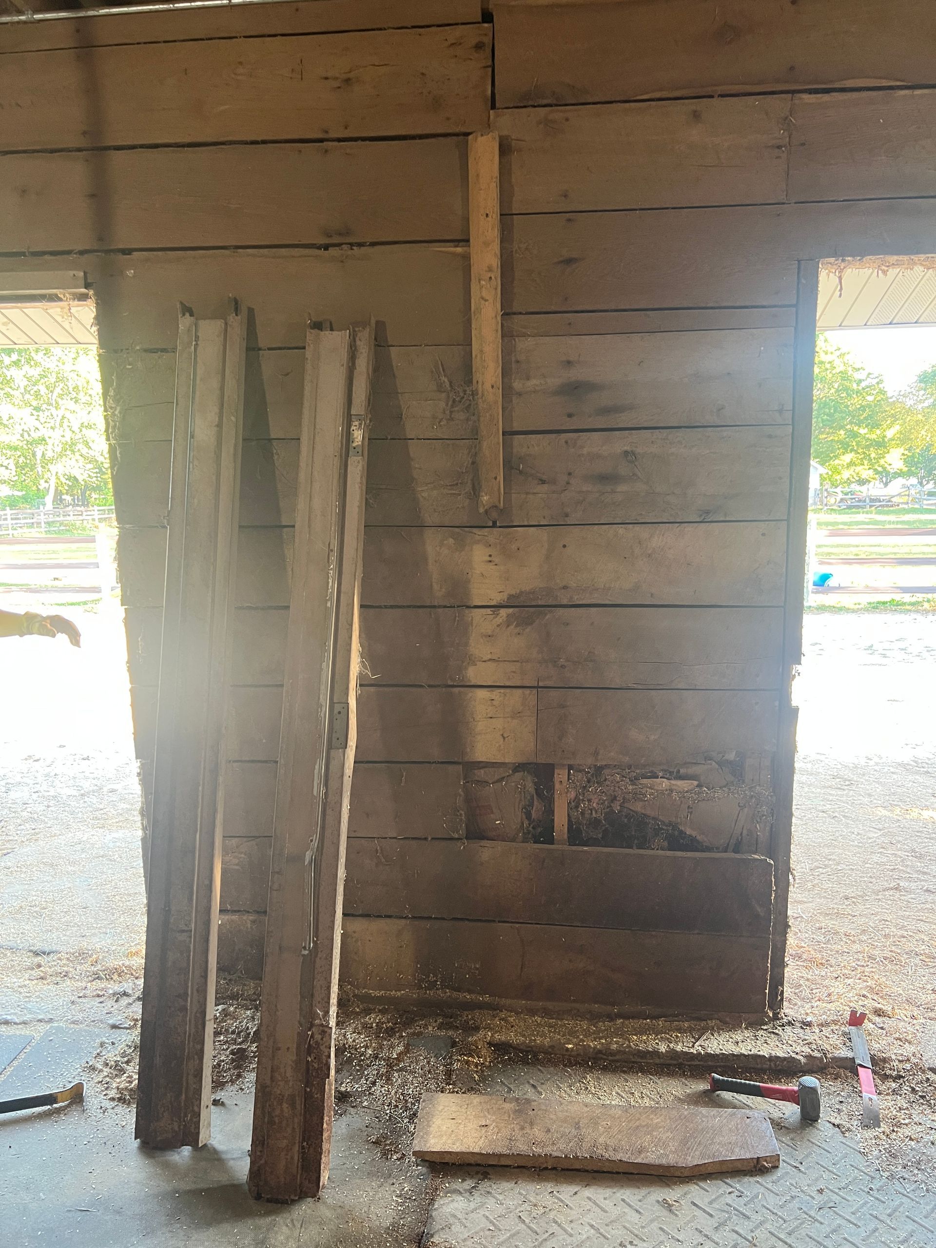 Two wooden boards lean against a rustic wall made of stacked horizontal planks with a section of missing wood.