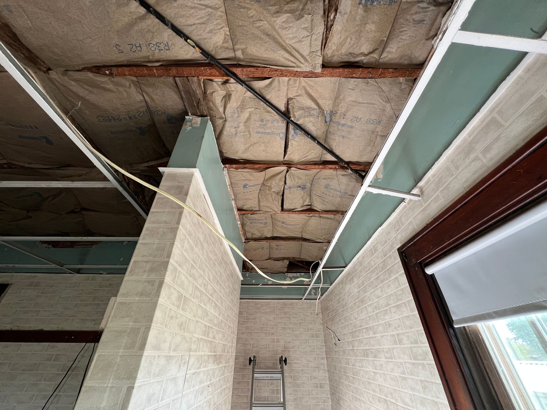 Low-angle view of a room under renovation with exposed ceiling insulation, unfinished walls, and a ladder in the distance.