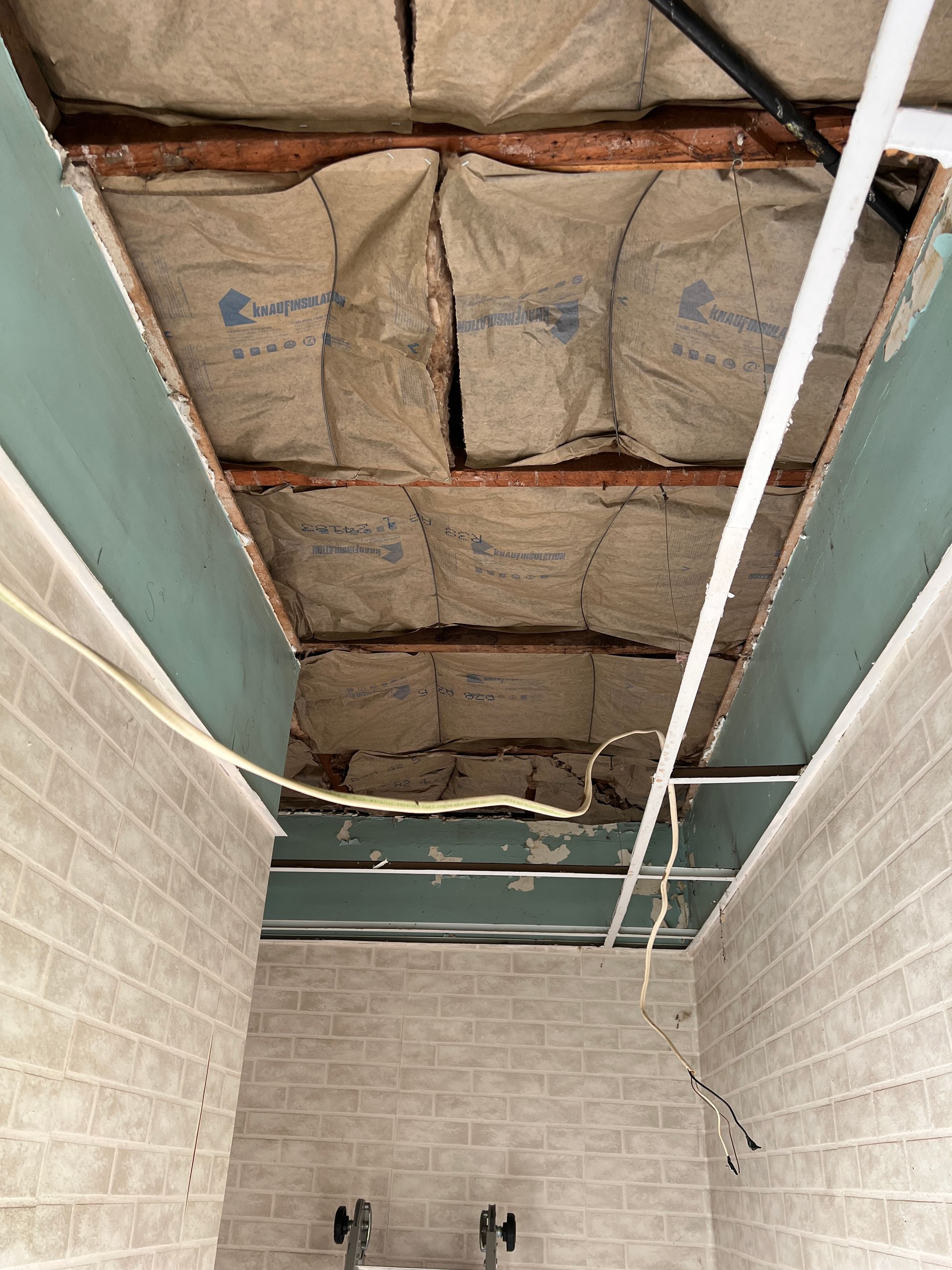 An interior view showing a partially finished ceiling with exposed wooden joists, insulation, and metal framing.