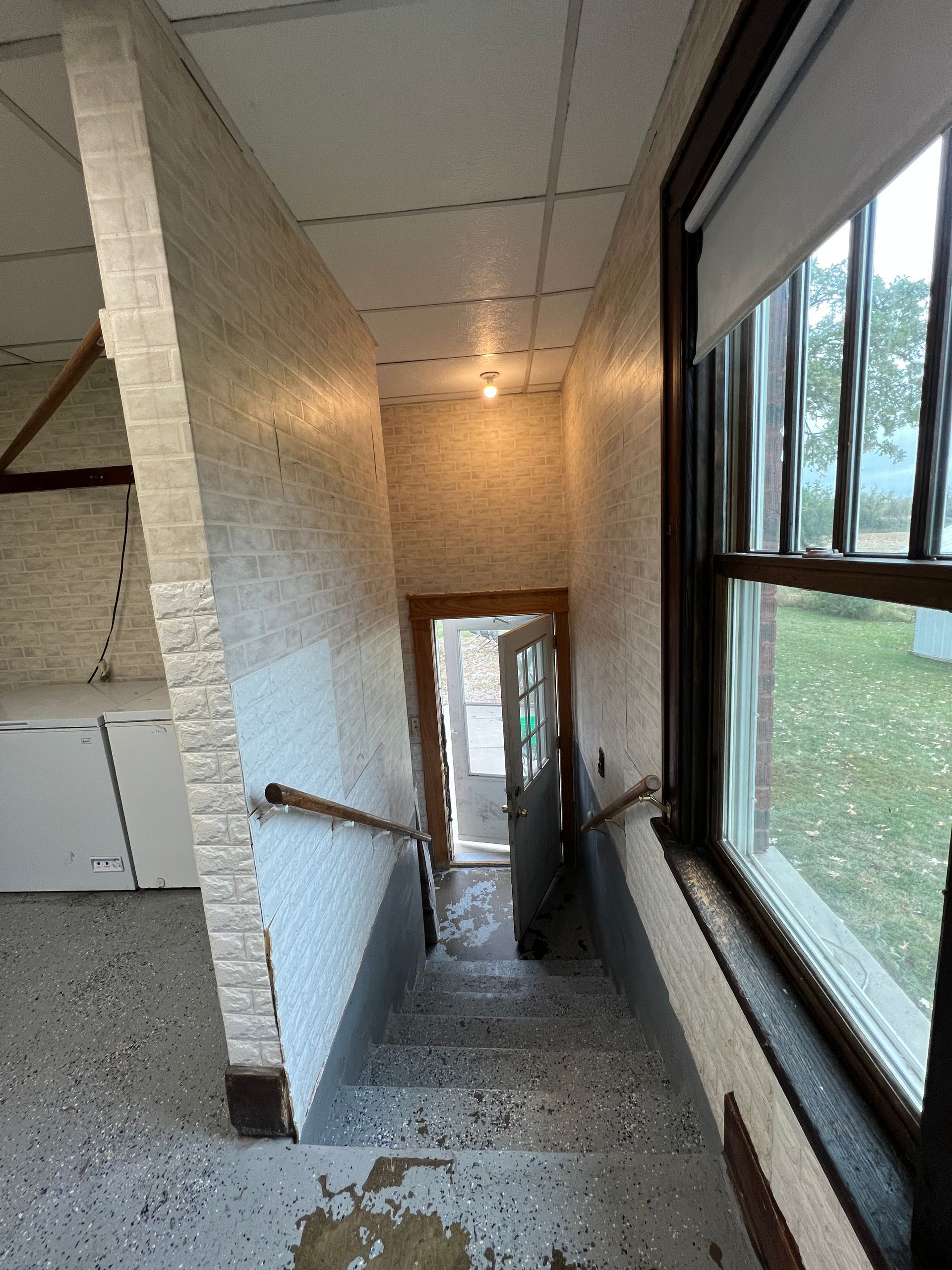 A view from the top of interior stairs leading down to an open door, with patterned walls and a large window to the right.