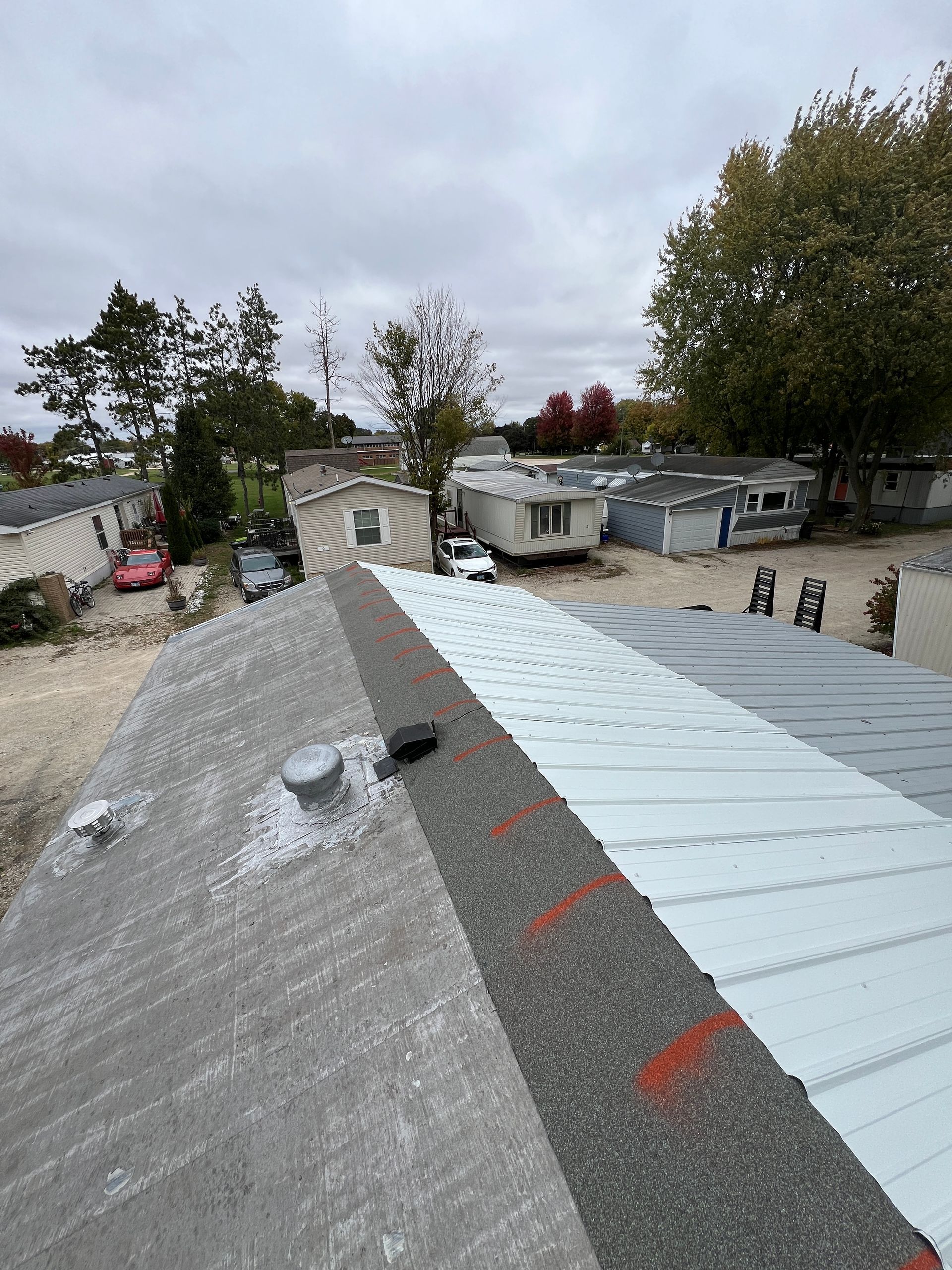 A high-angle view of a manufactured home roof featuring patches of weathered shingles and new metal roofing sections.