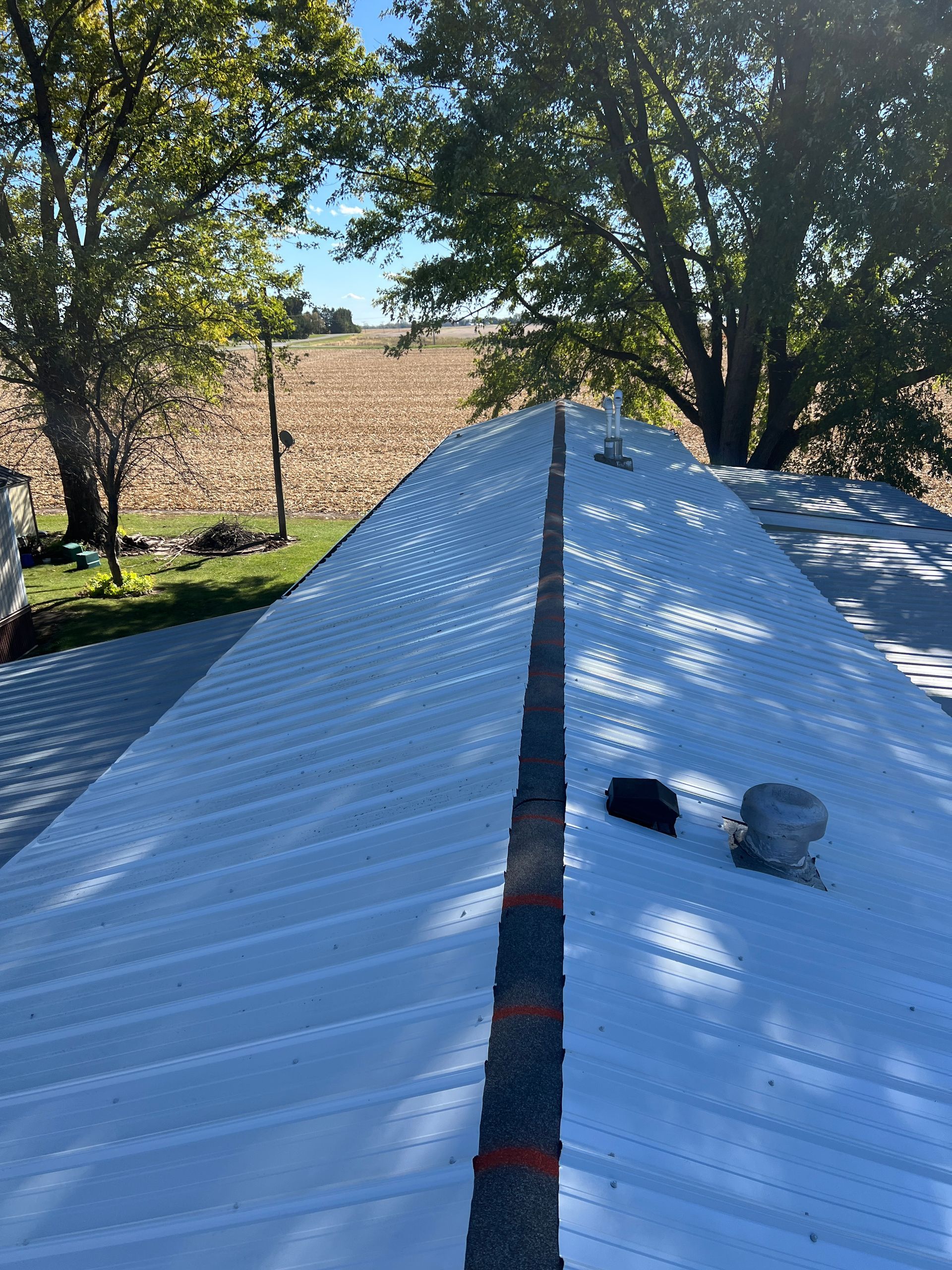 A view looking down the peak of a white metal roof towards a field and trees under a clear blue sky.