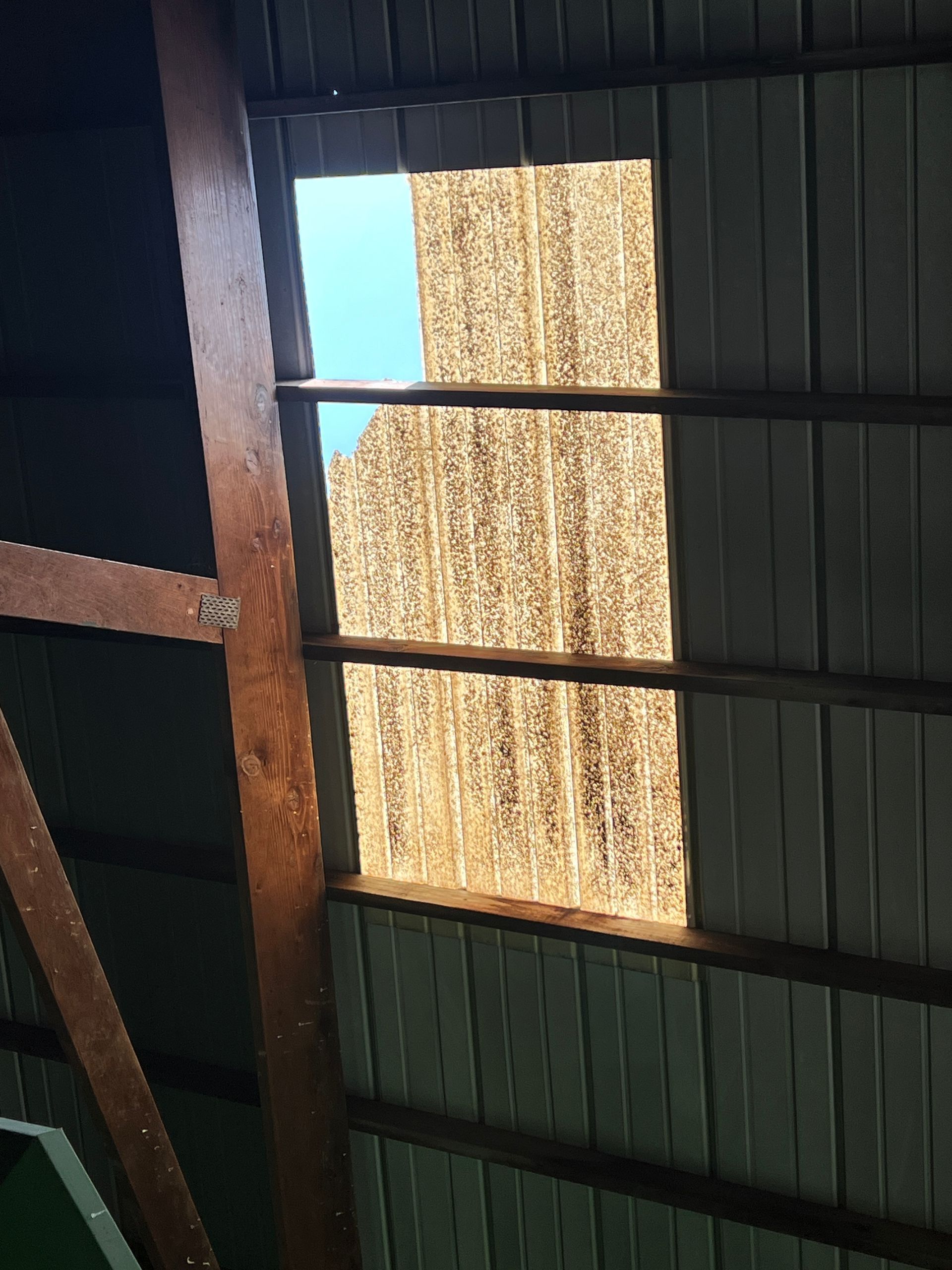 Looking up at a damaged corrugated metal roof, showing a rectangular section of sky through a hole.