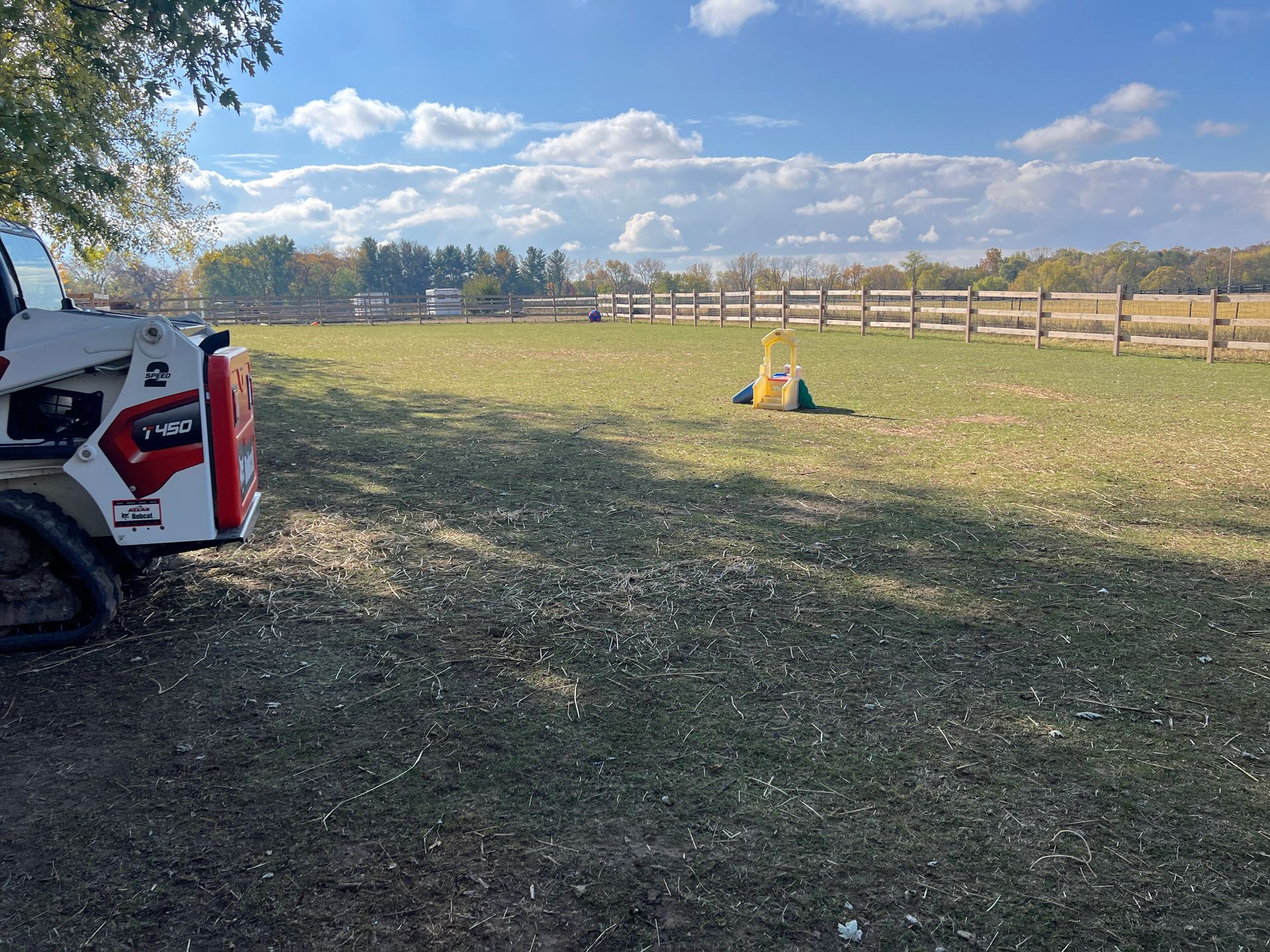 A white and red Bobcat skid-steer parked on a grassy field with a yellow lawn tool nearby under a bright, cloudy sky.