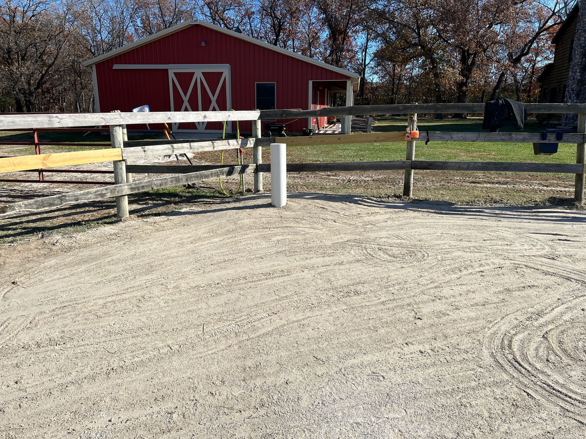 A gravel area with a wooden fence and a red barn in the background under a blue sky.