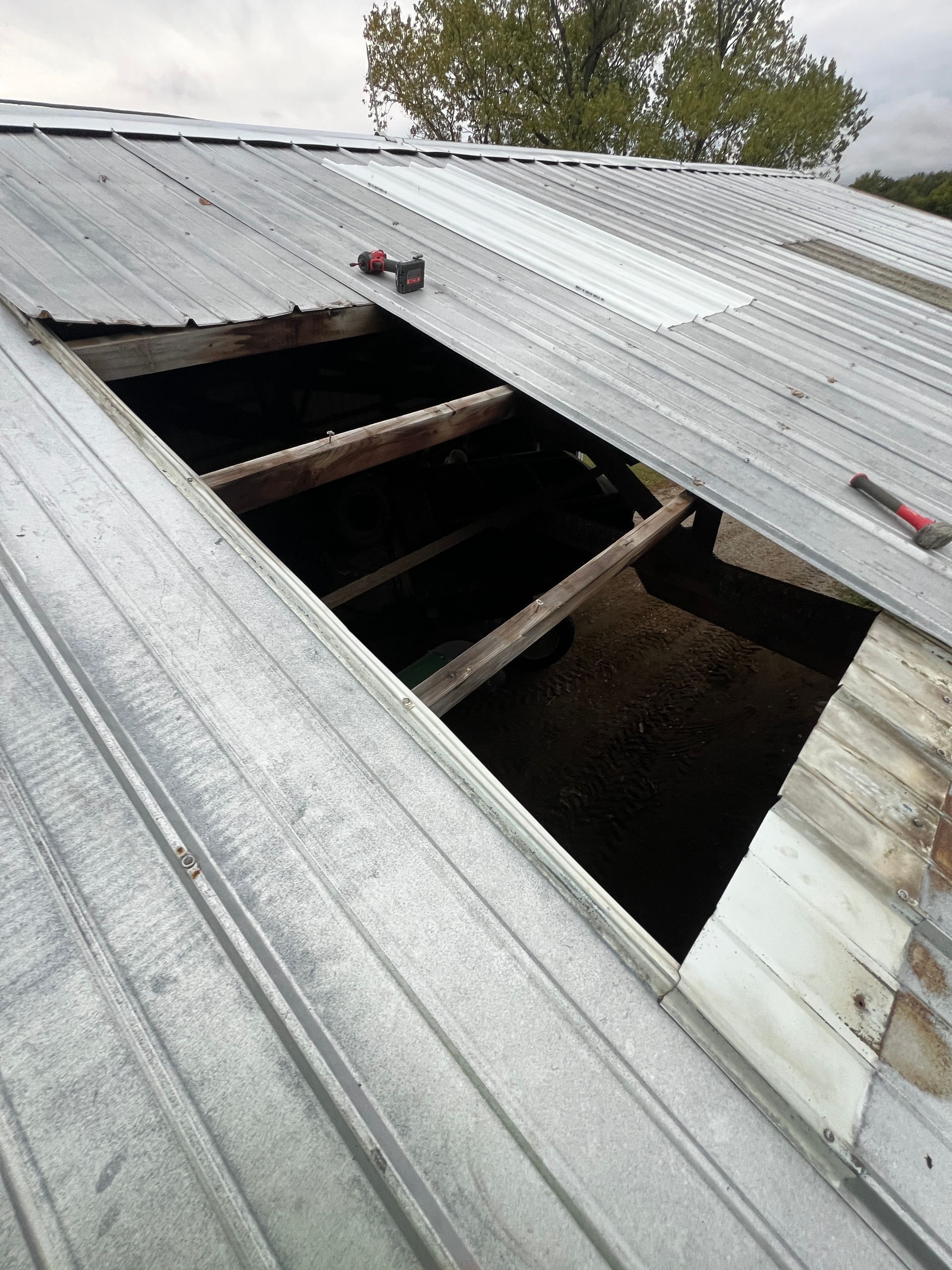A metal roof with a large rectangular opening, showing exposed wooden support beams against an outdoor background.