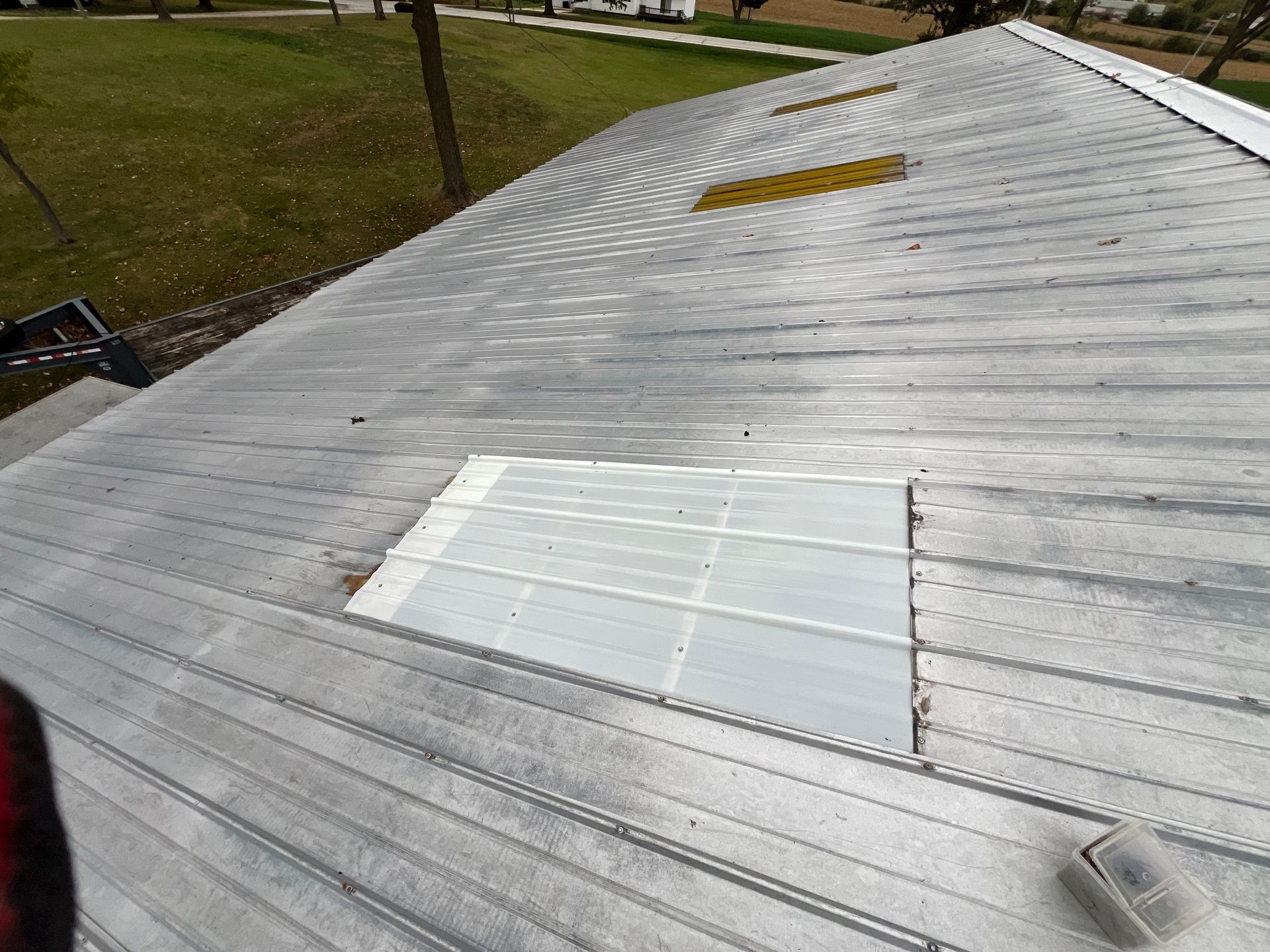 A corrugated metal roof featuring two translucent skylights, set against a grassy, outdoor background.