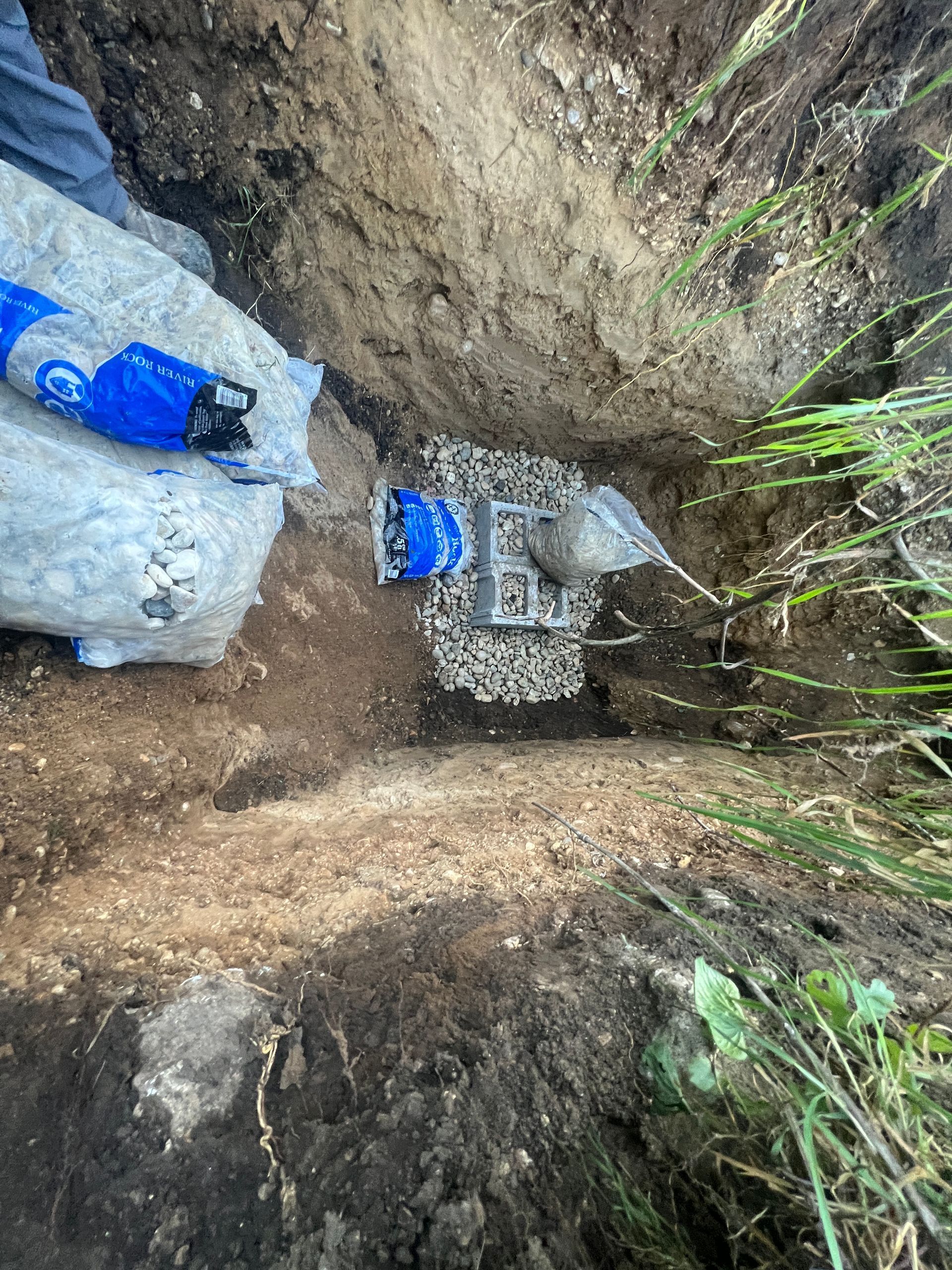 An open trench containing a metal utility fixture, gravel, and blue protective packaging for an underground installation.