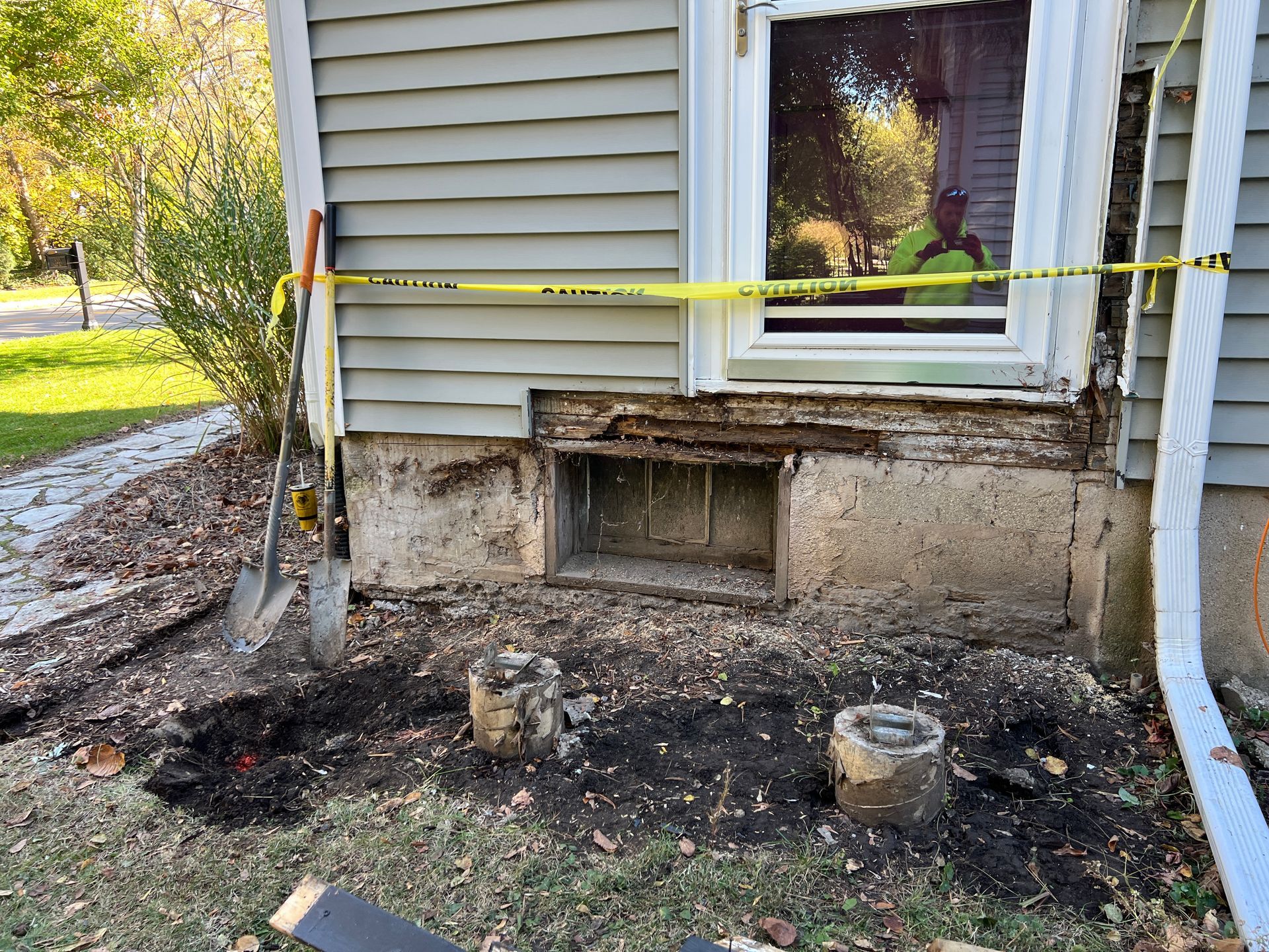 A house exterior with damaged, rotting wood framing beneath a window, marked off by yellow caution tape.