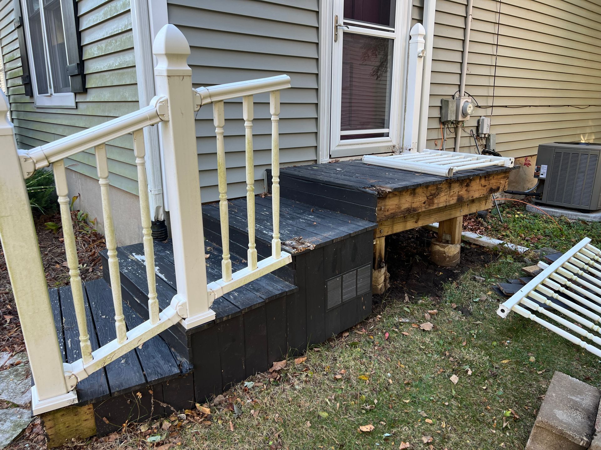 A set of exterior stairs with a white railing leading to a house door, with exposed wood framing and detached lattice.