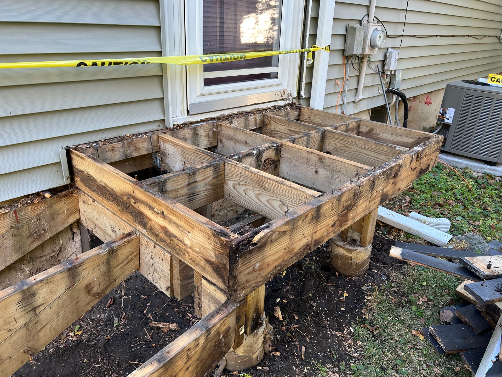 Wooden deck framing under construction attached to the side of a house with yellow caution tape across the doorway.