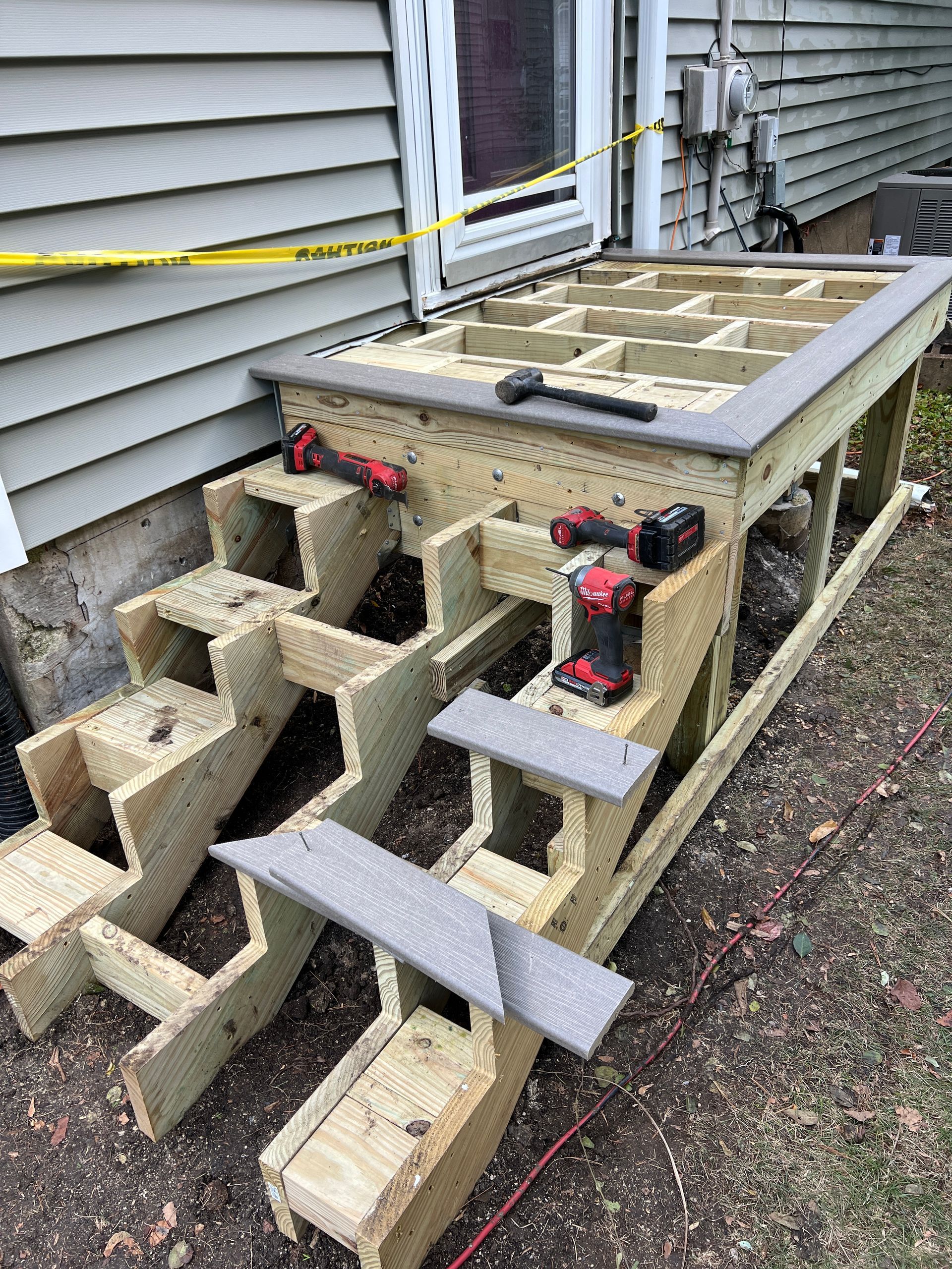 A partially constructed wooden deck and staircase with grey composite trim, located outside a house with siding.