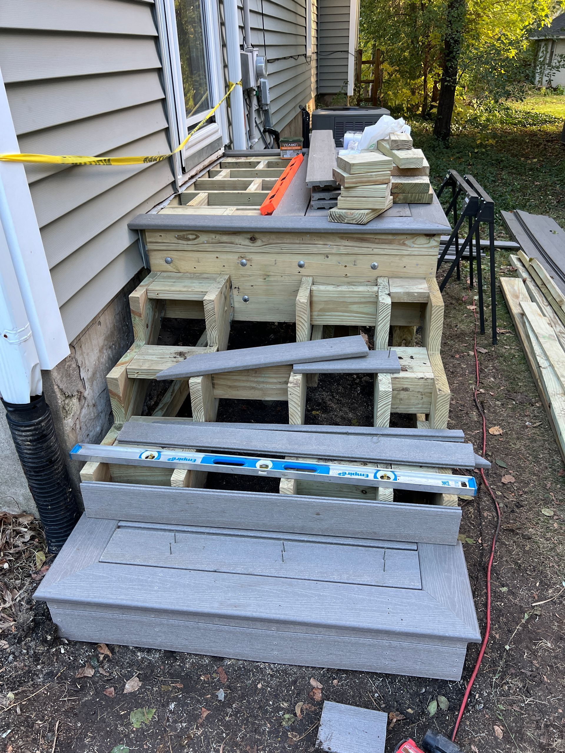 Wooden deck stairs under construction with gray composite treads and an orange level placed on top.