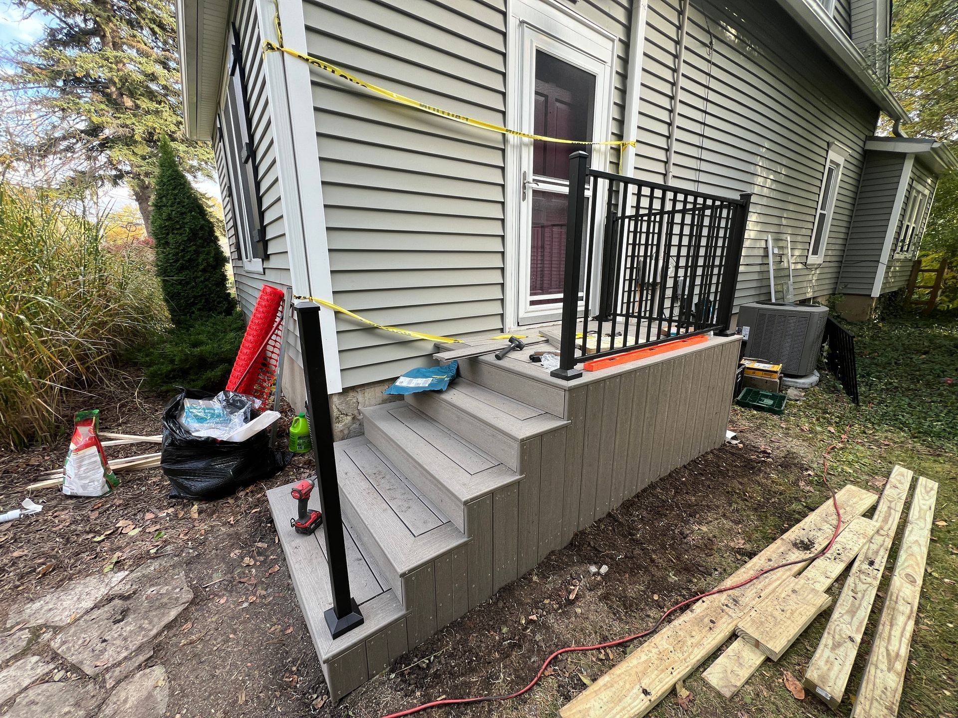 Newly installed grey exterior steps with black metal railings in front of a house, marked off with yellow caution tape.
