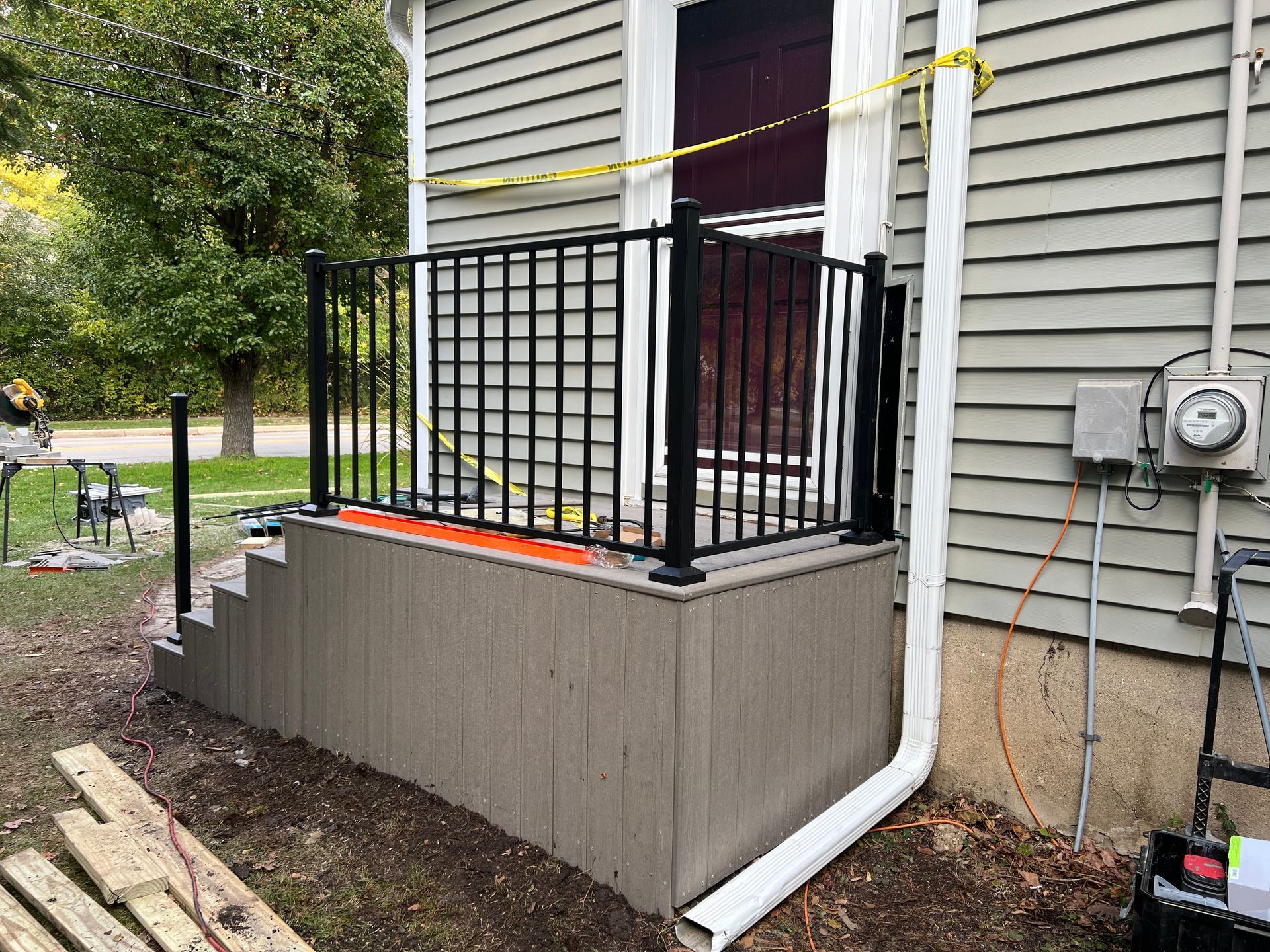 A small, newly constructed porch with tan siding and black metal railings sits beside a home with a white downspout.