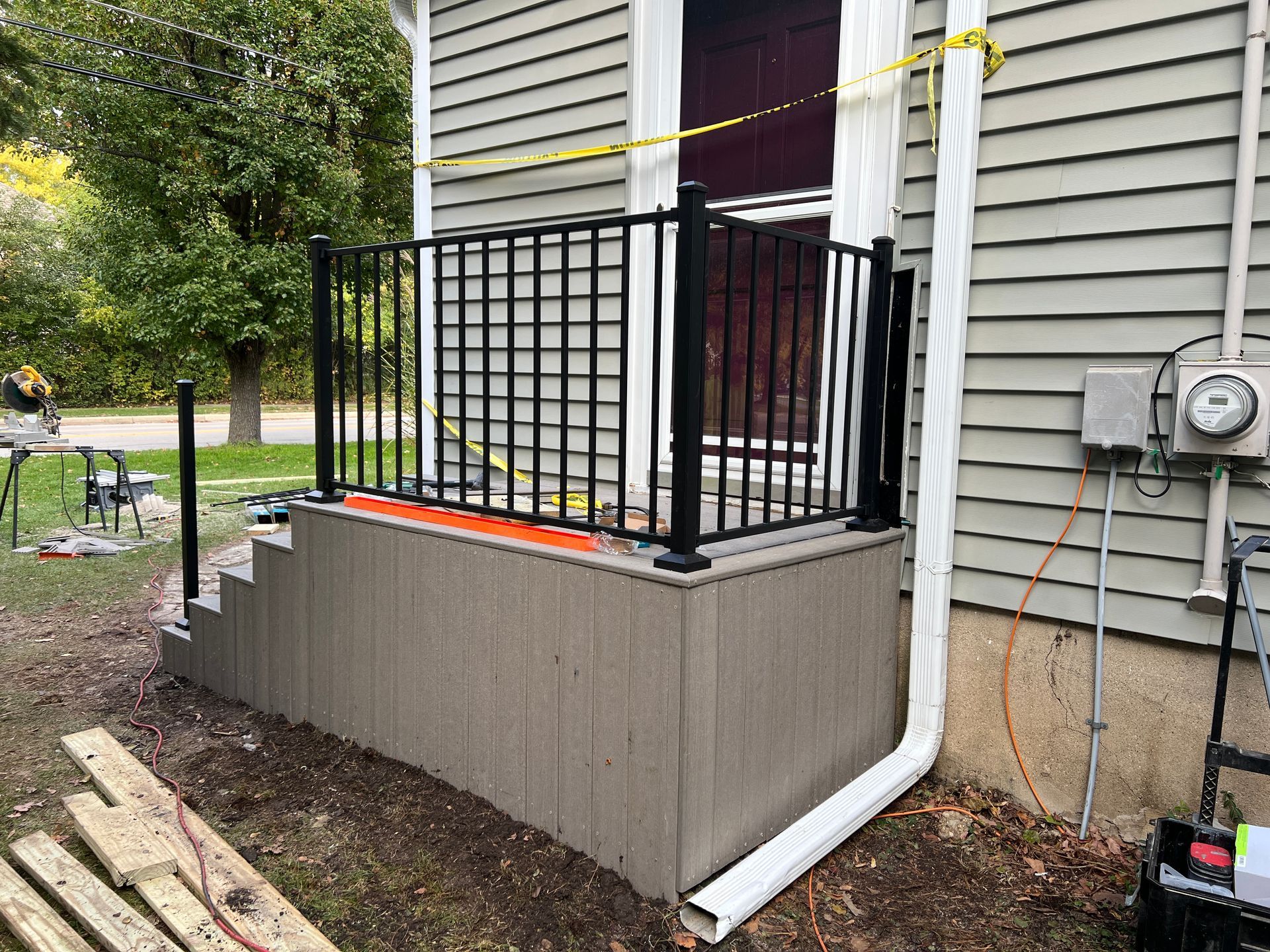 Newly built wooden deck platform with black metal railing and matching stairs attached to the side of a light gray house.