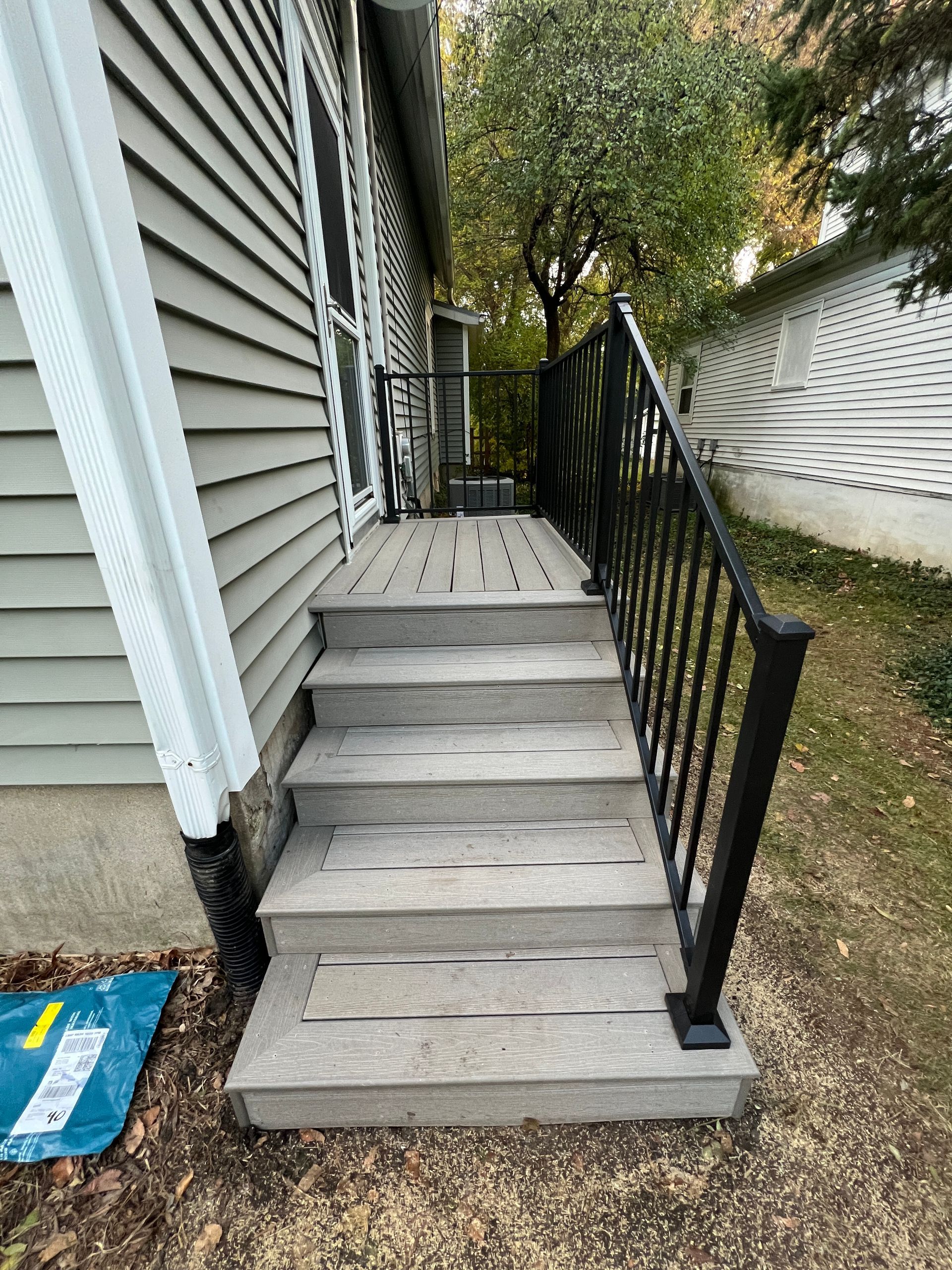 Outdoor light gray composite steps leading to a side door with black metal railings, set against a house with siding.
