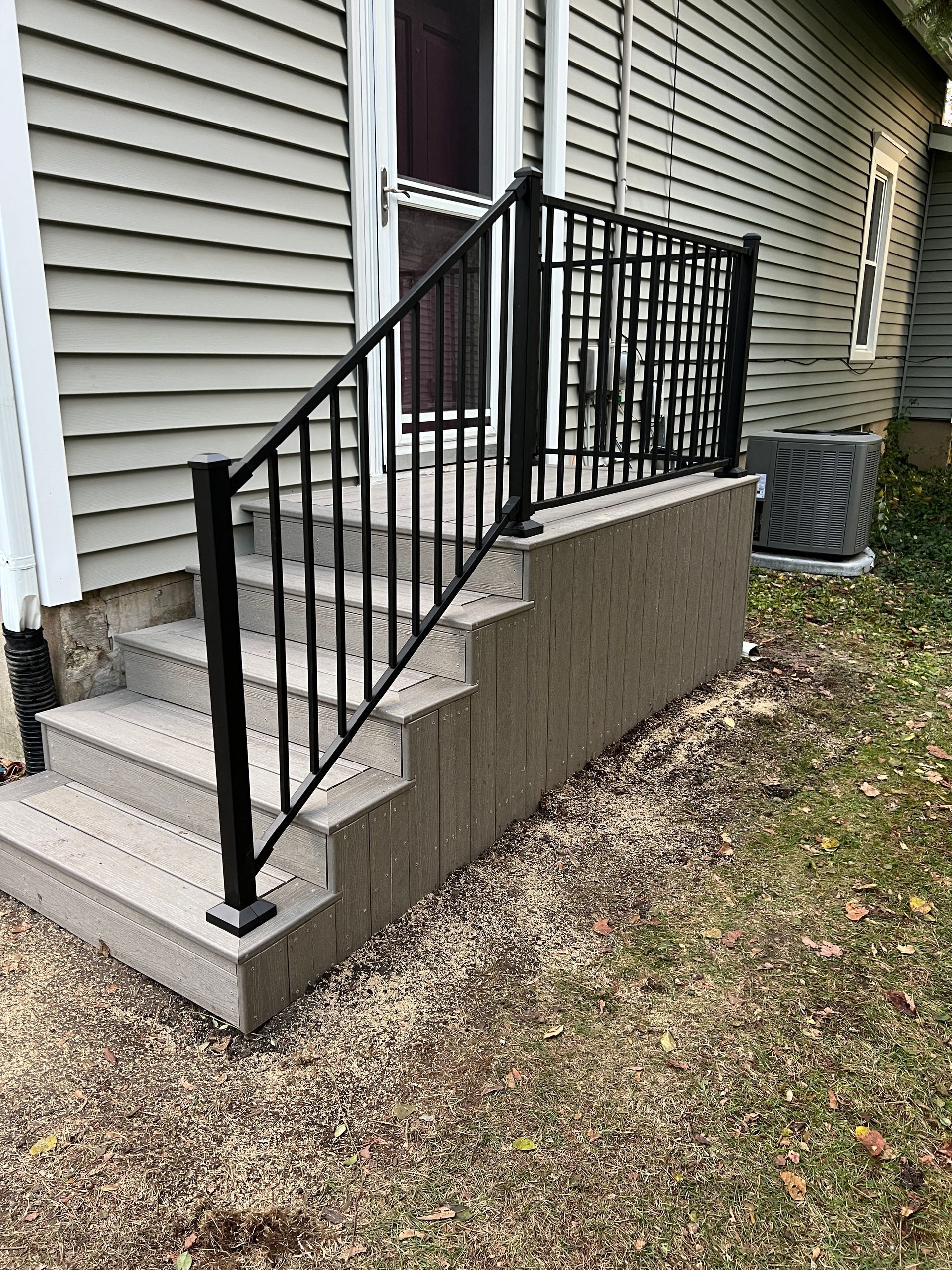 Exterior concrete stairs with black metal railings leading to a house entrance.