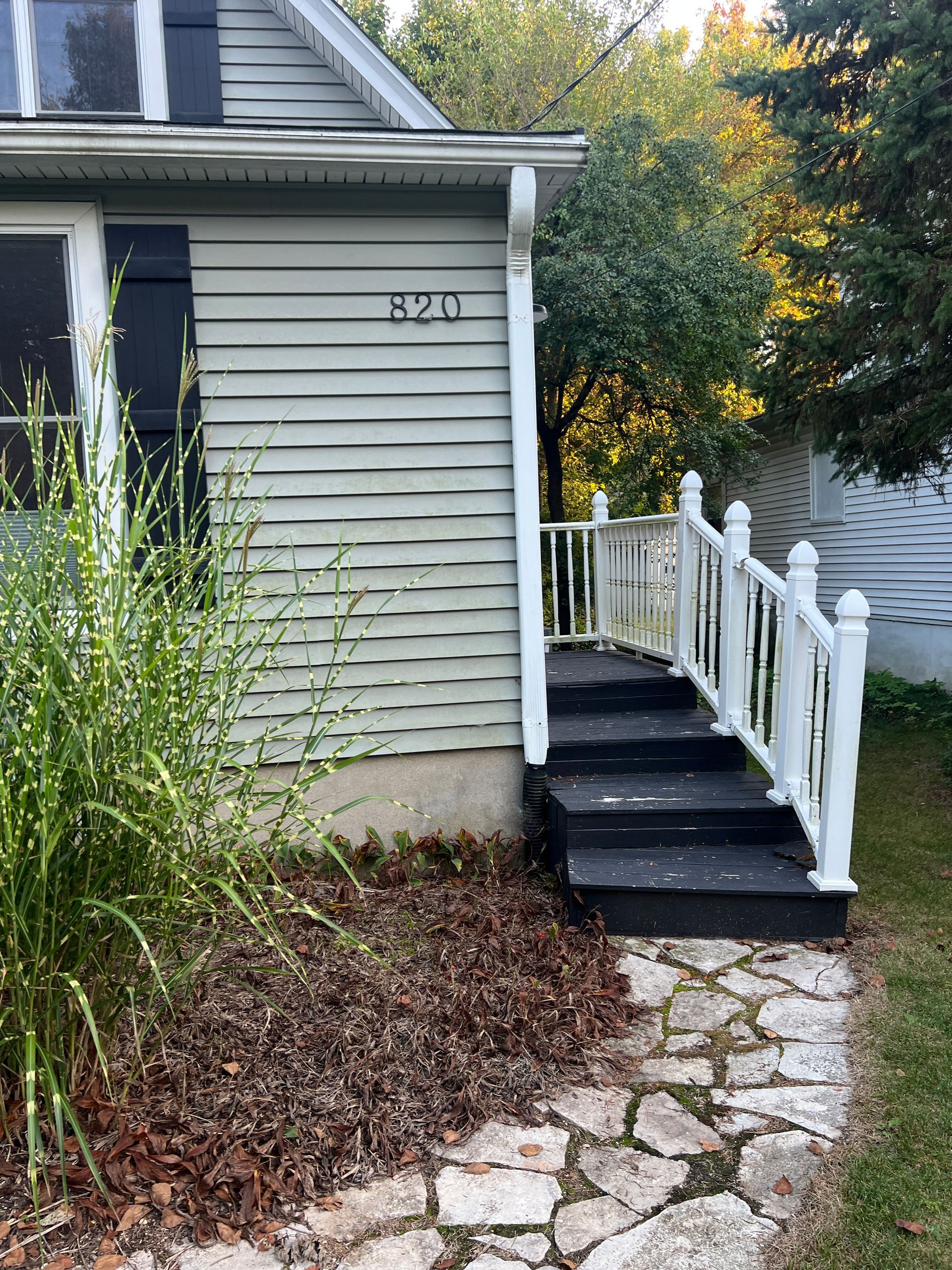 A grey house with the number 820 features black front steps and a white railing leading to an entrance.