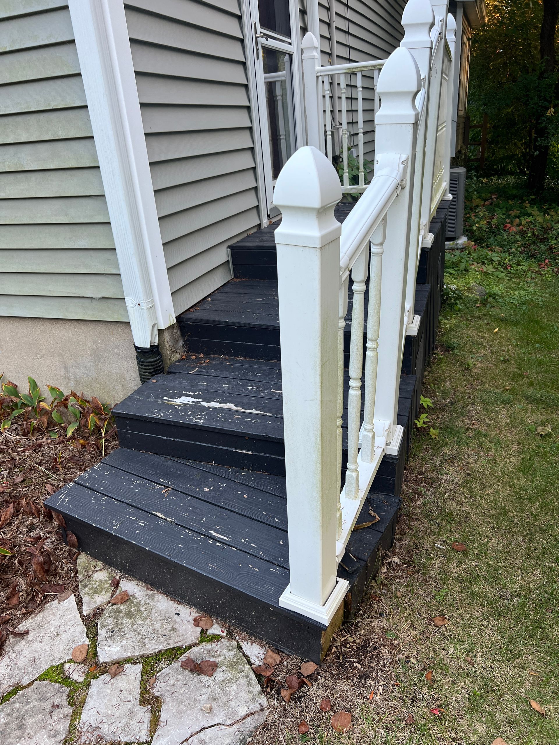 Outdoor steps with black treads, white railings, and a small landing, situated next to a house with beige siding.