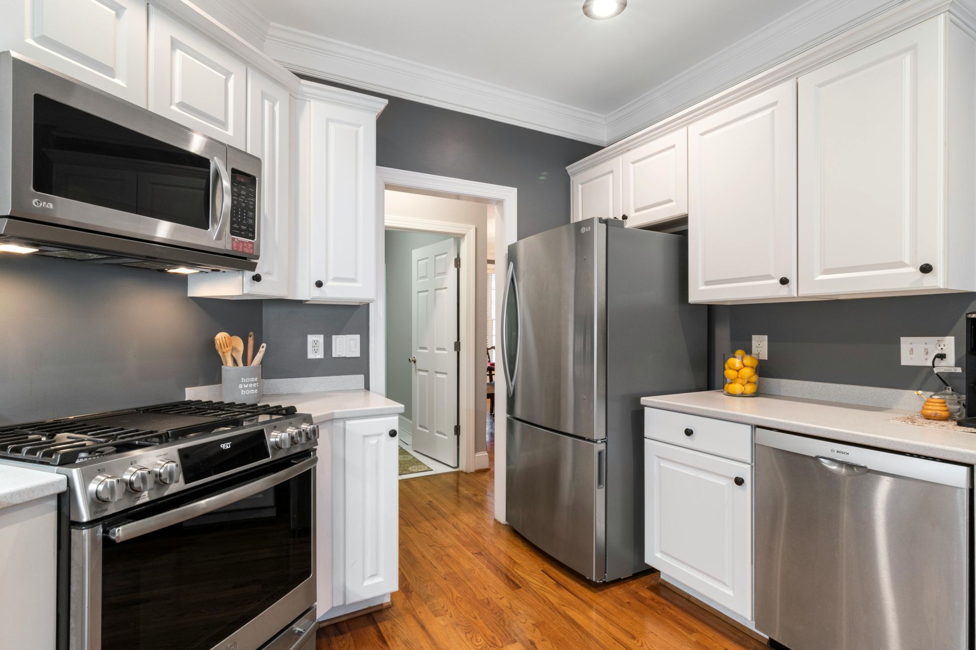 A modern kitchen featuring white cabinets, stainless steel appliances, dark grey walls, and hardwood floors.
