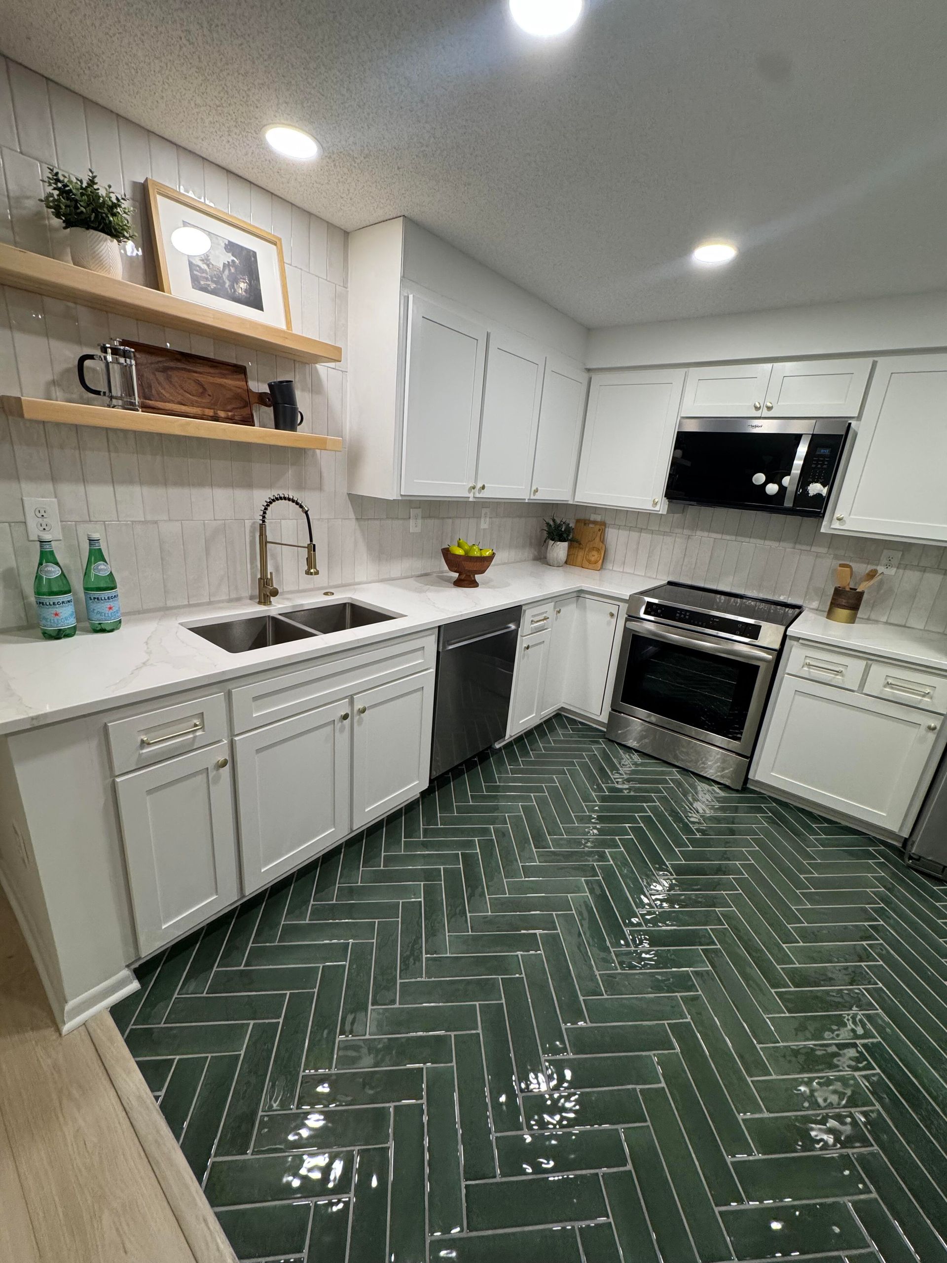 Green herringbone tile kitchen floor, white cabinets, stainless steel appliances, and wood open shelves.