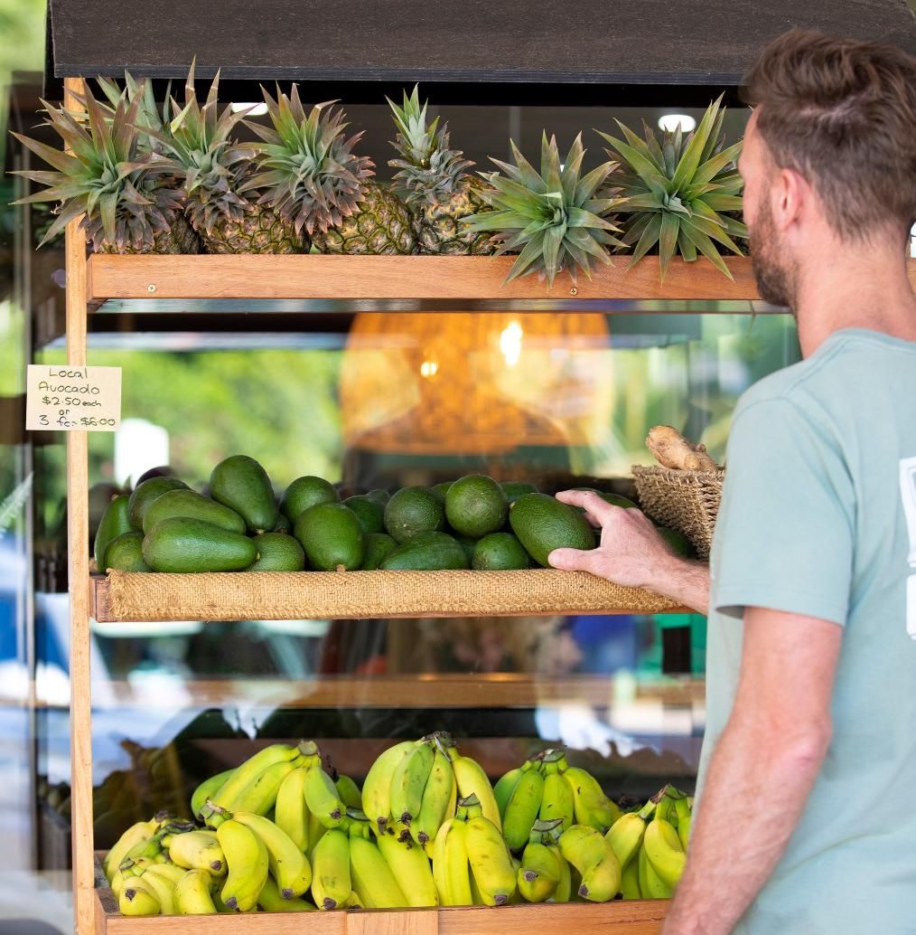 A Man Is Standing In Front Of A Display Of Bananas And Pineapples — The Real Grocer In Golden Beach, QLD