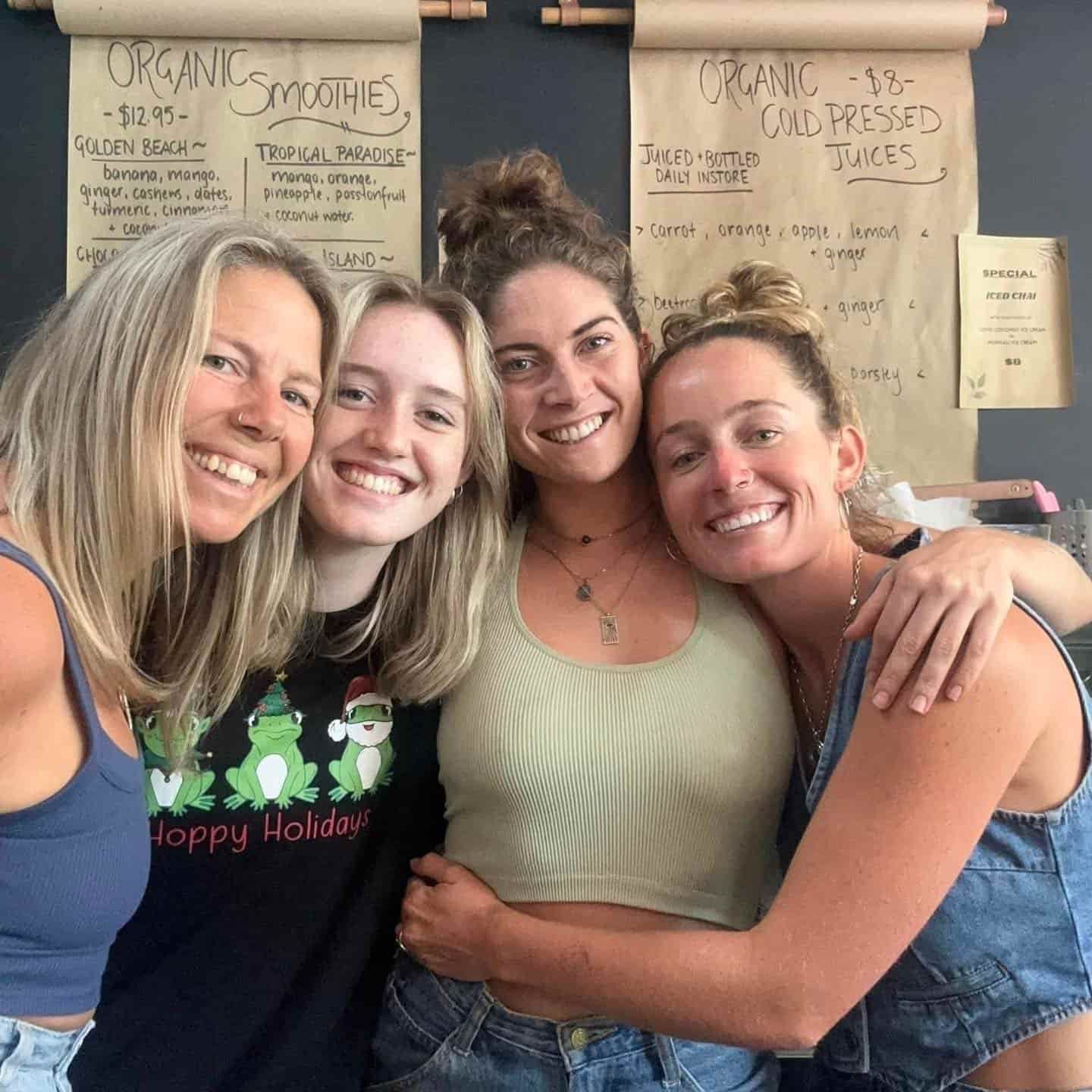 A Group Of Women Are Posing For A Picture And One Of Them Is Wearing A Shirt That Says Happy Holiday — The Real Grocer In Golden Beach, QLD
