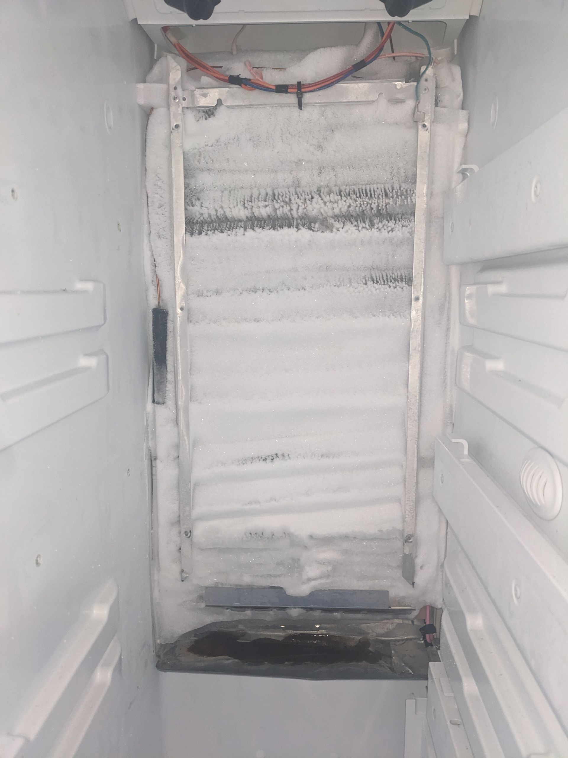 Frozen, frost-covered refrigerator interior with an icy back wall and dark bottom tray