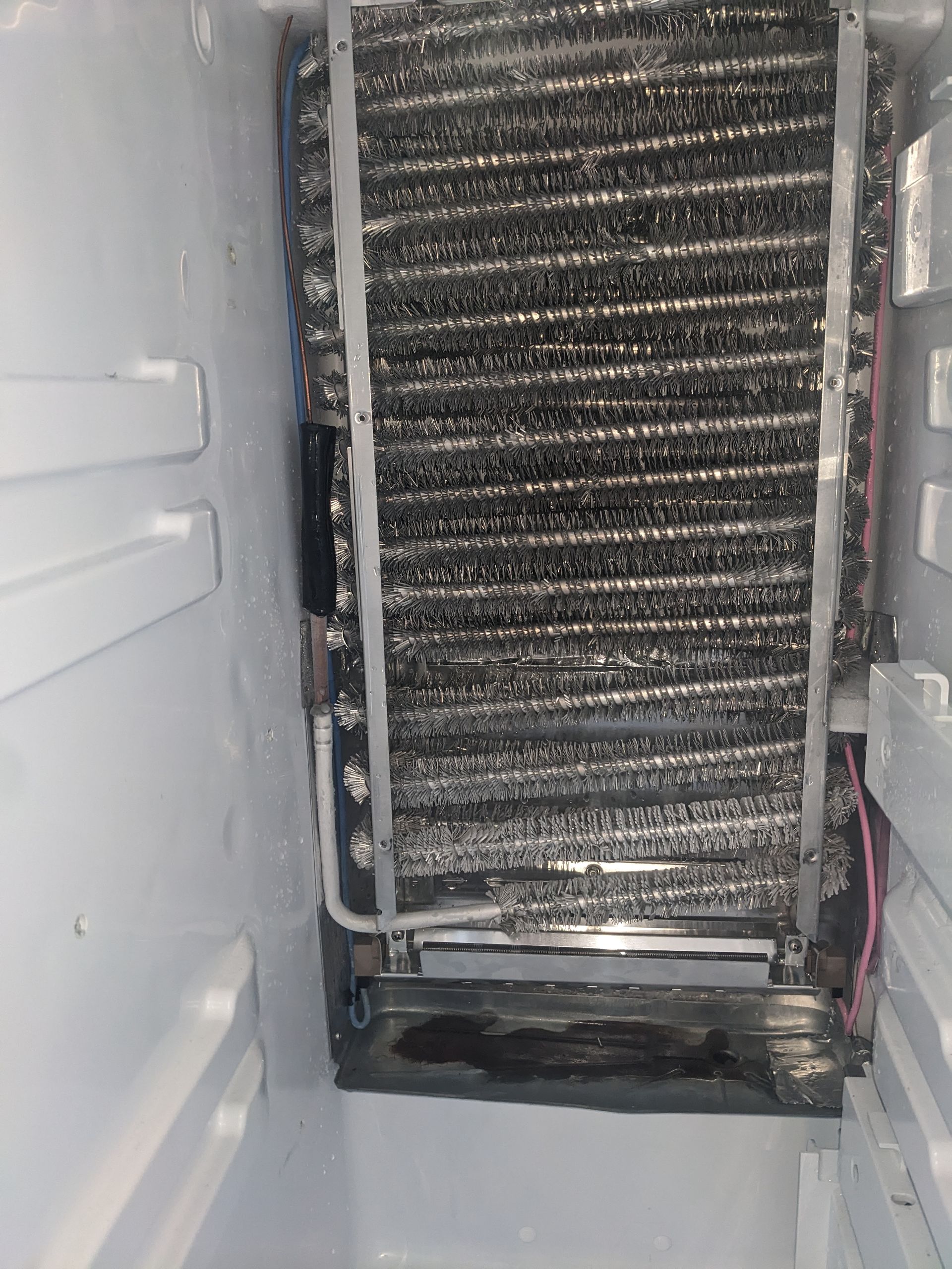 Close-up of a refrigerator cooling coil with frost buildup and white interior panels