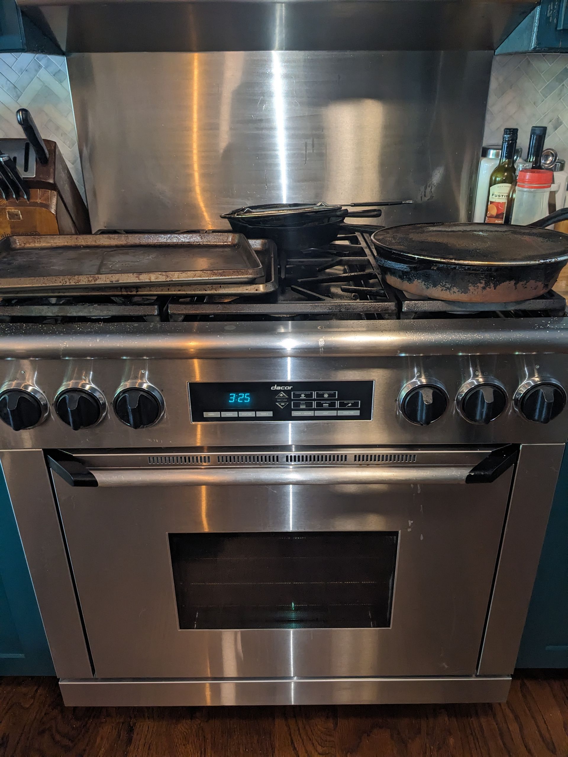 Stainless steel gas oven with blue digital display and two pans on the stovetop in a kitchen