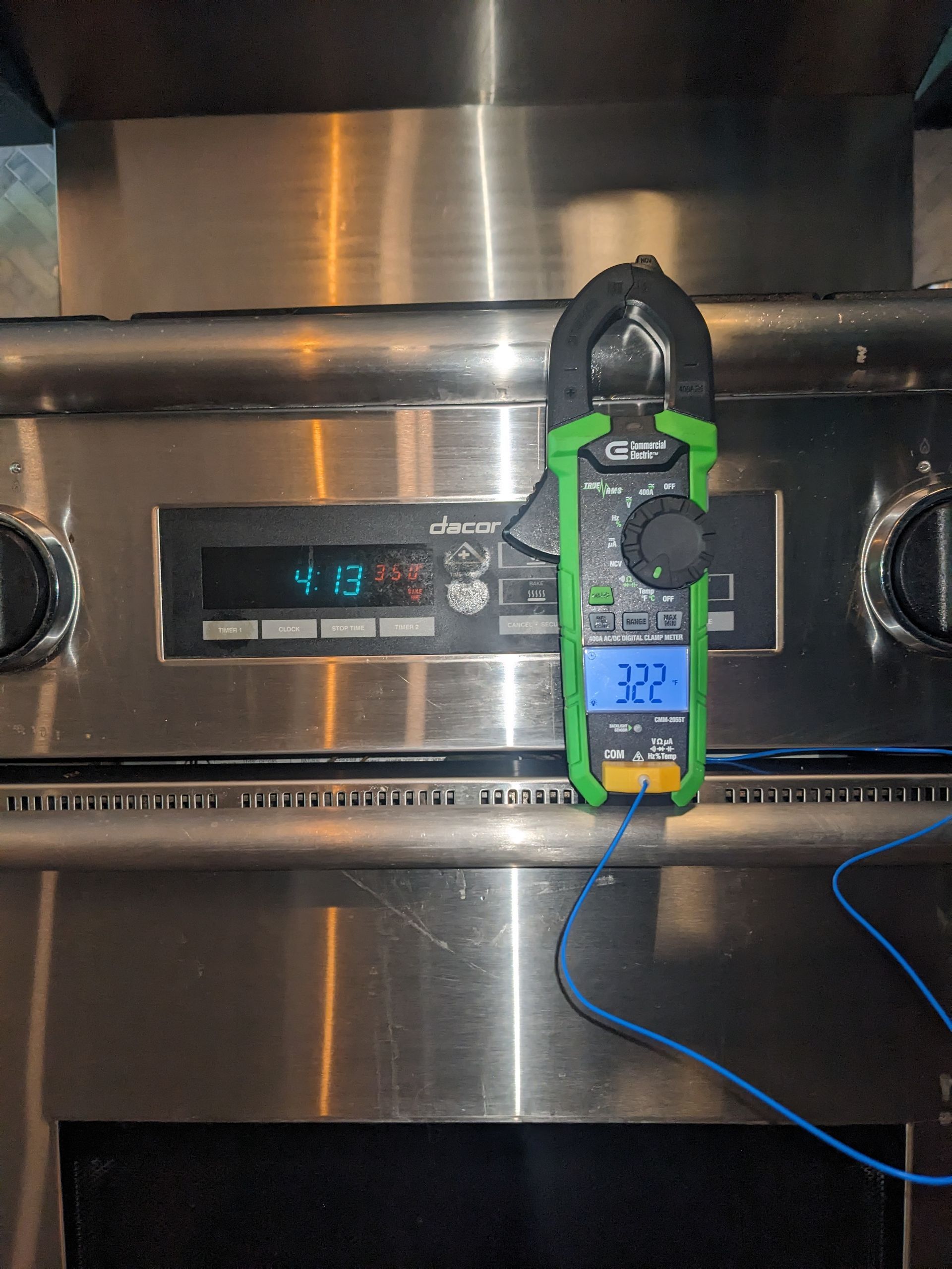 Stainless steel oven control panel with a green clamp meter and blue cord hanging in front of it
