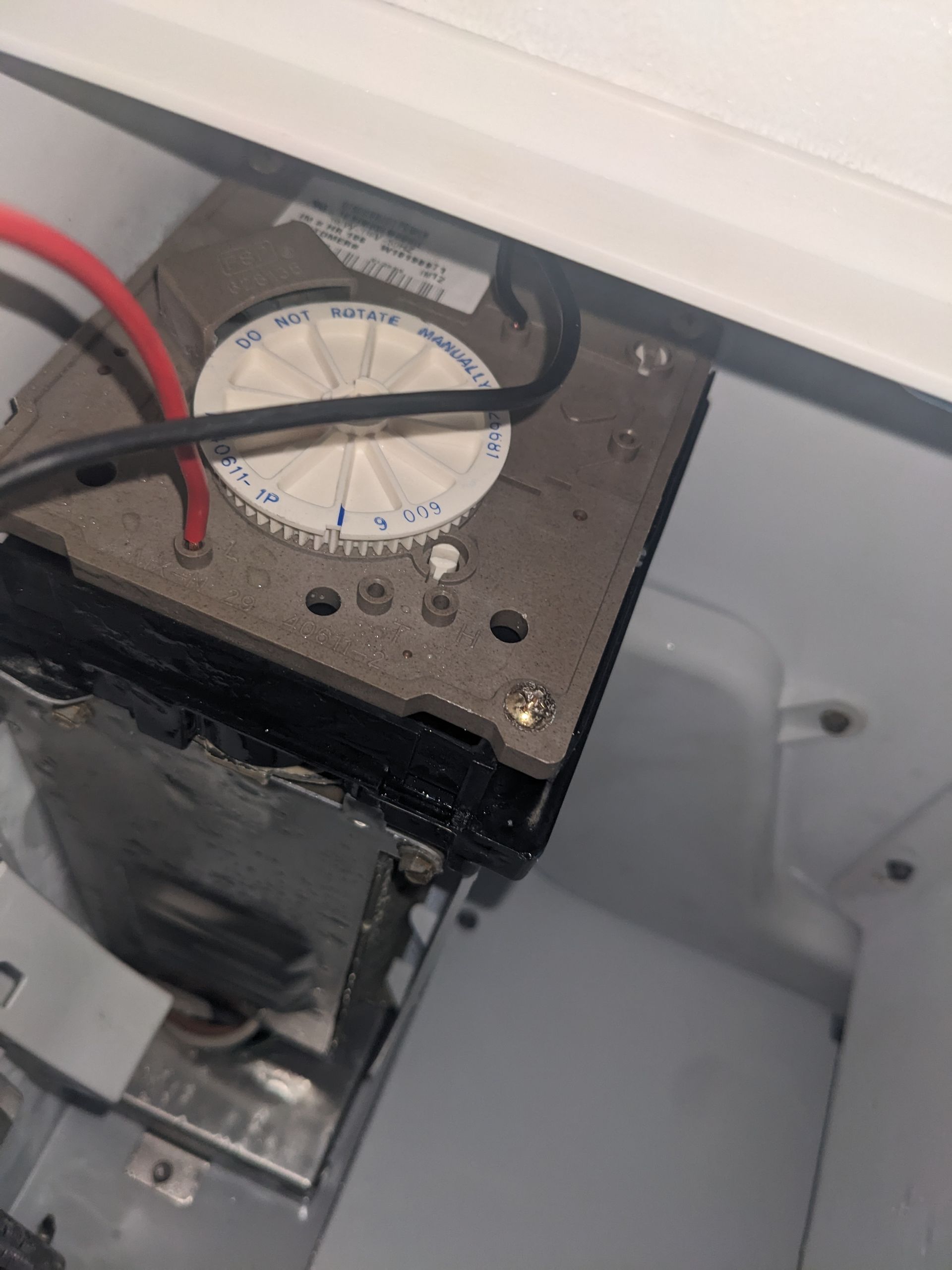 Close-up of a dirty electrical control box with a round dial and red and black wires inside a white cabinet