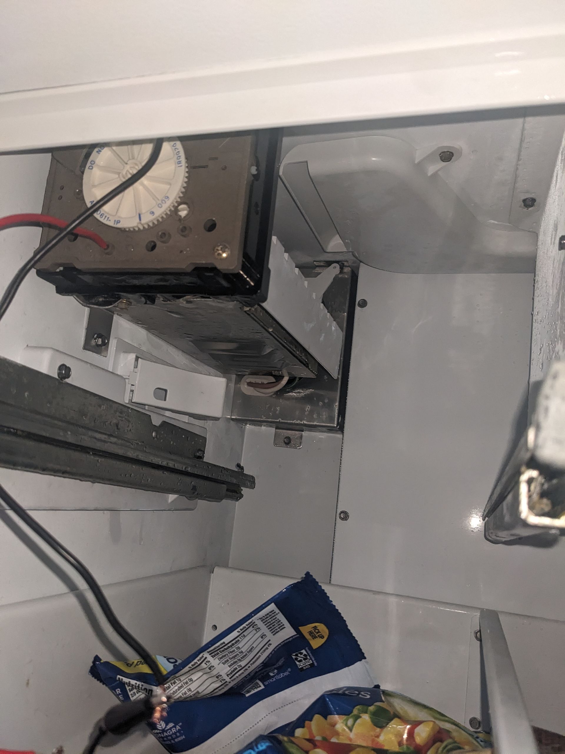 Under-counter view of a stainless appliance and wiring, with a blue package lying on the floor.