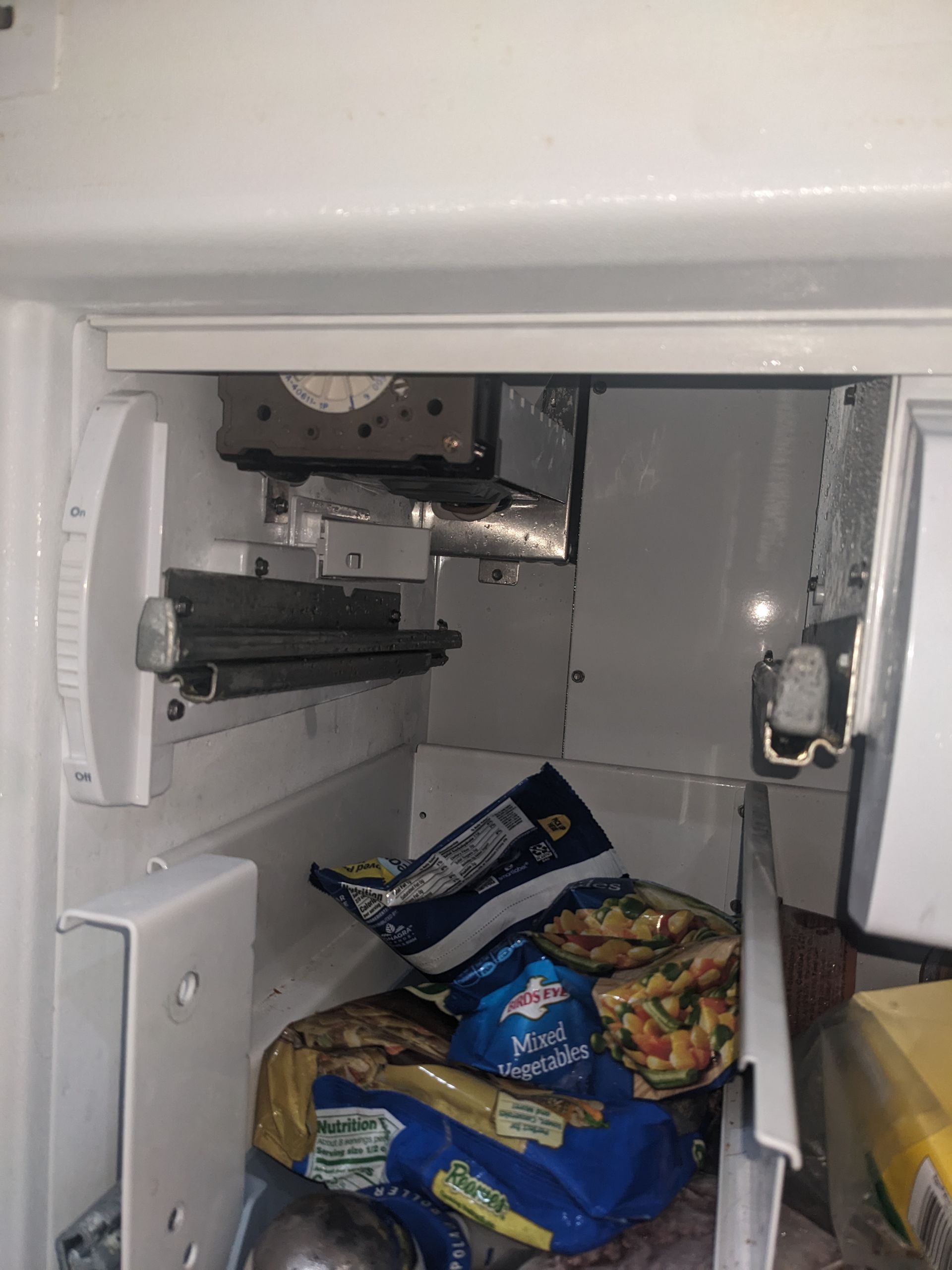 Open freezer with frozen food packages inside and exposed mechanical parts at the top