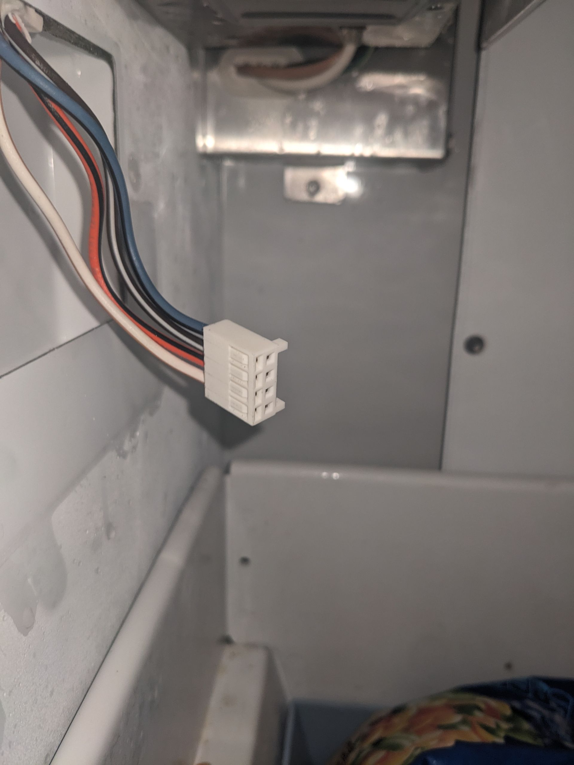 White electrical wire connector hanging inside a metal appliance panel.