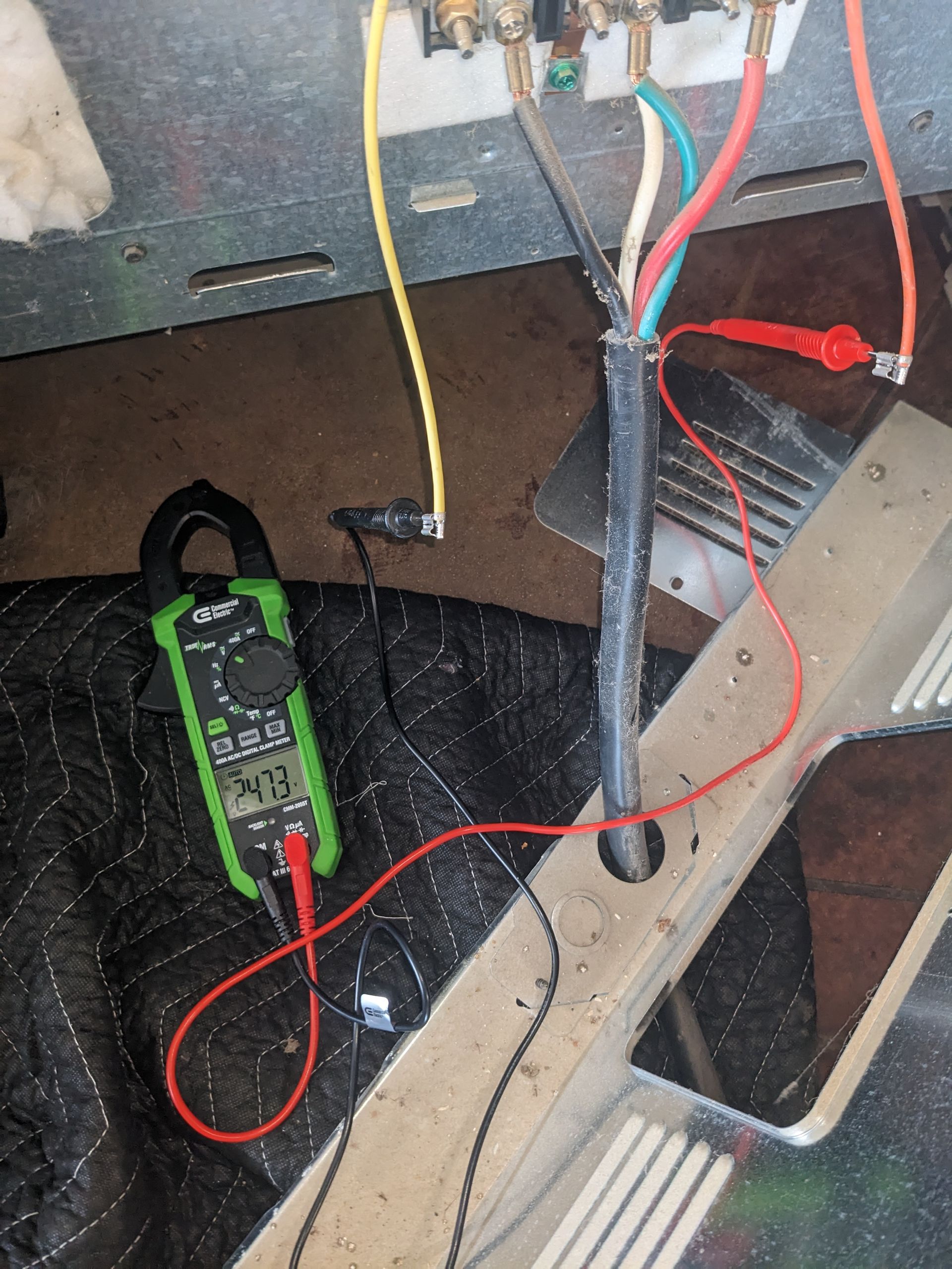 Cluttered floor with a green clamp meter, red and black leads, and exposed wiring near a metal frame