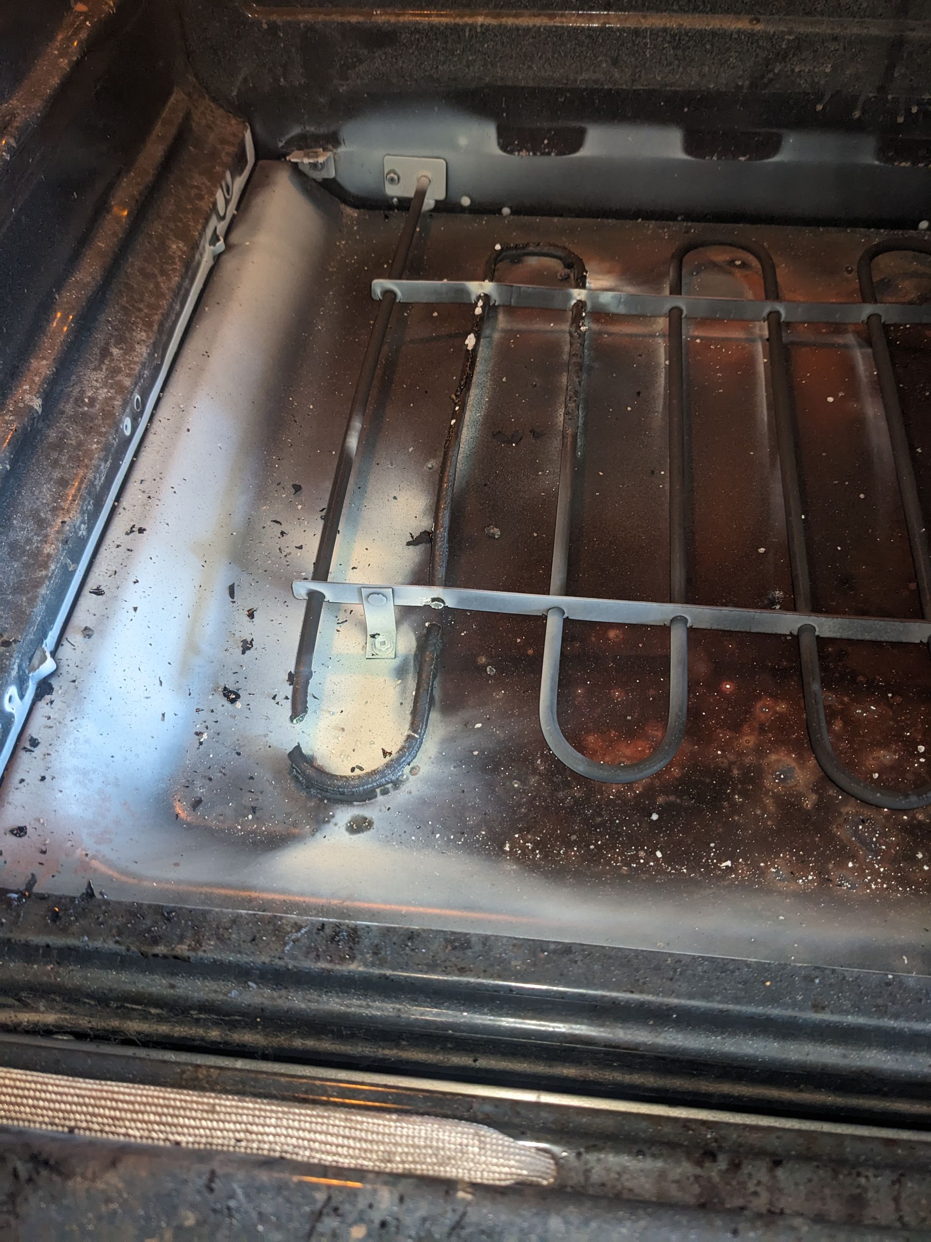 Dirty oven interior with spilled crumbs and a baking rack.